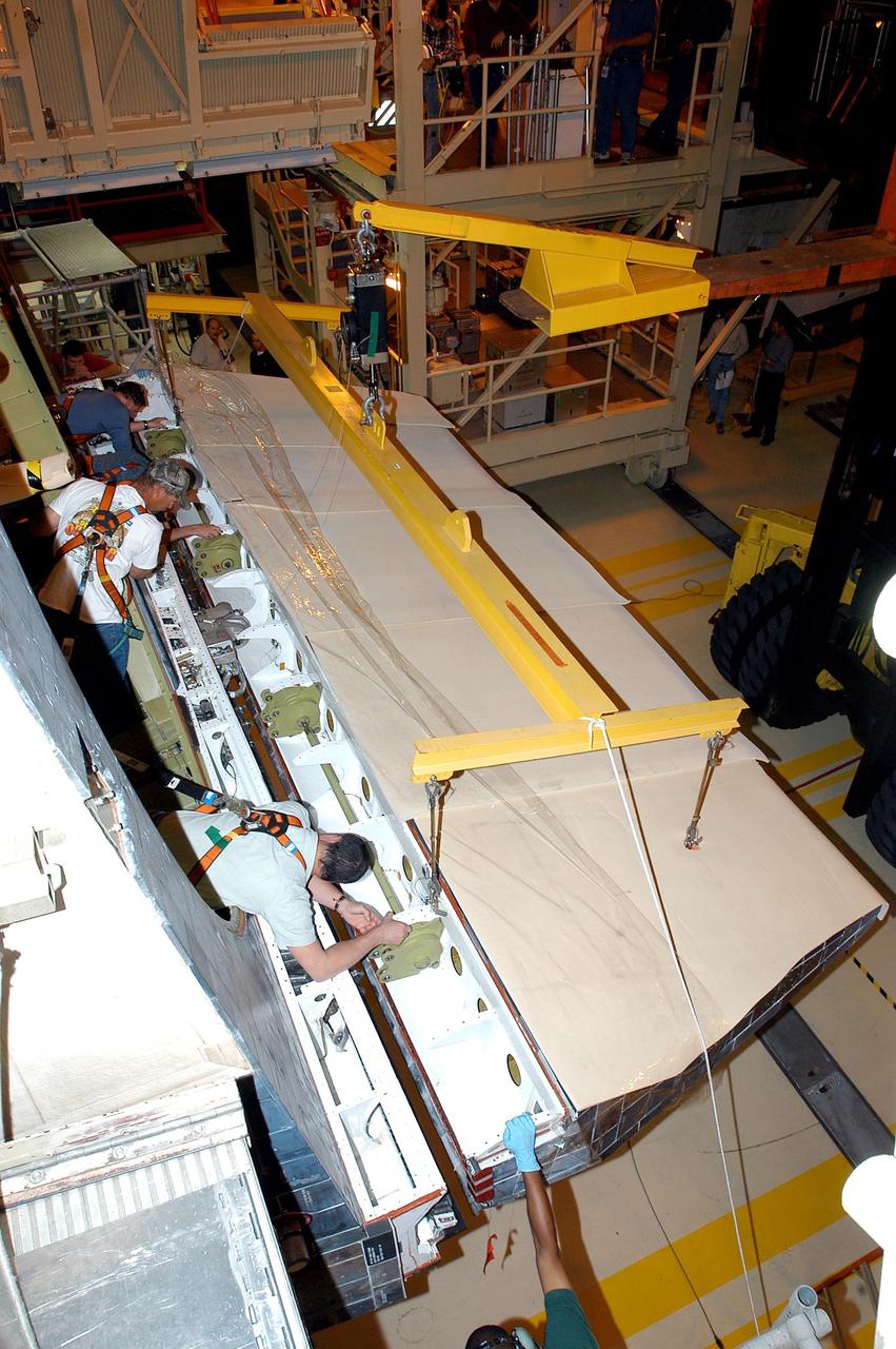 KENNEDY SPACE CENTER, FLA. -  Workers in the Orbiter Processing Facility help move the body flap into position on the orbiter Discovery.  The body flap is an aluminum structure consisting of ribs, spars, skin panels and a trailing edge assembly. It thermally shields the three main engines during entry and provides pitch control trim during landing approach.  Discovery is being processed for launch on the first Return to Flight mission, STS-114.