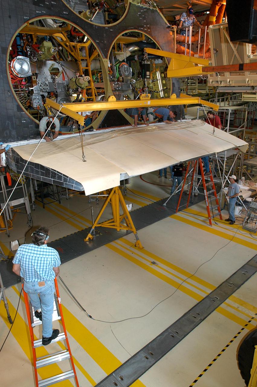 KENNEDY SPACE CENTER, FLA. -  A worker on a ladder (lower left) observes installation of the body flap onto the orbiter Discovery. The body flap is an aluminum structure consisting of ribs, spars, skin panels and a trailing edge assembly. It thermally shields the three main engines during entry and provides pitch control trim during landing approach. Discovery is being processed for launch on the first Return to Flight mission, STS-114.