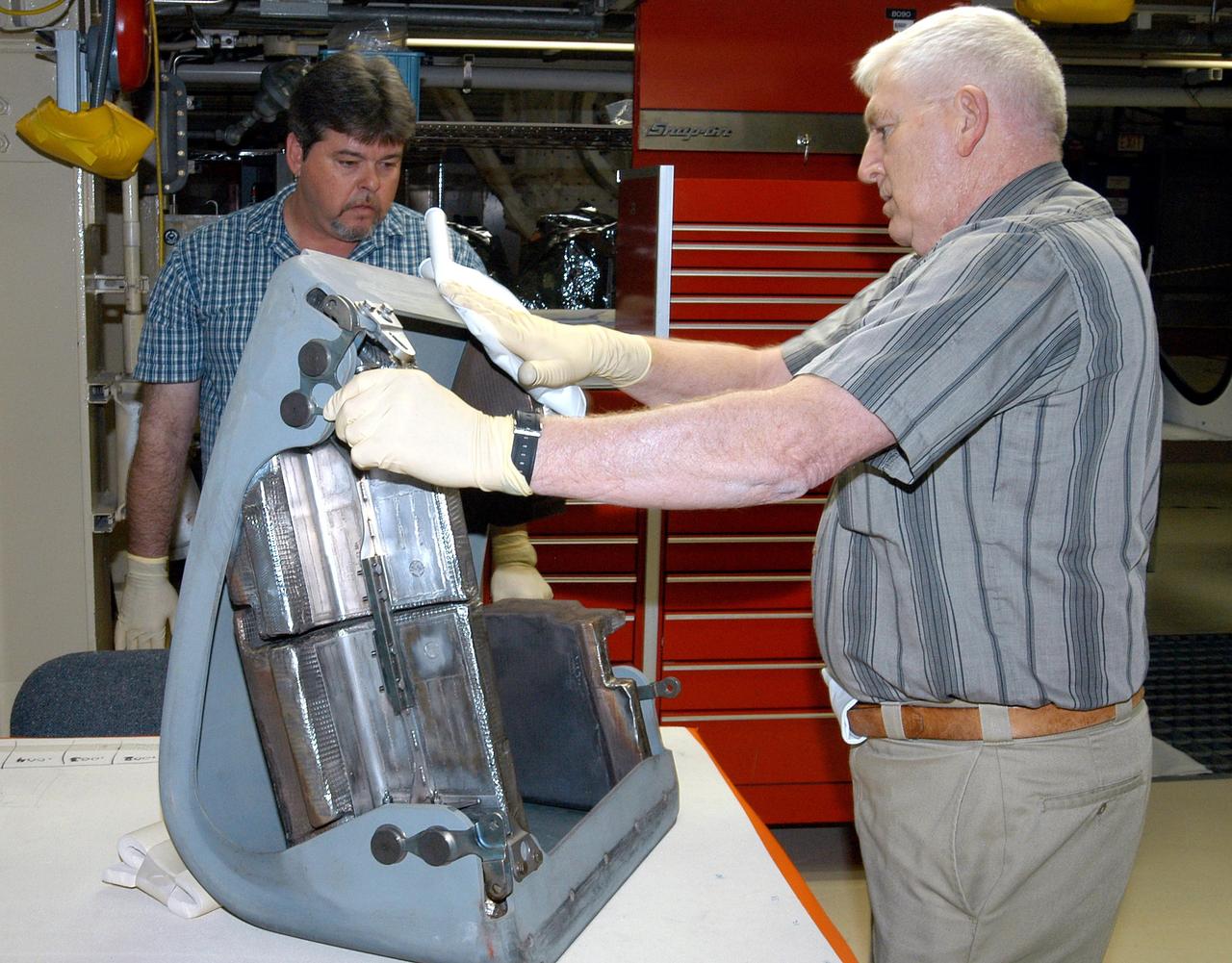 KENNEDY SPACE CENTER, FLA. -  In the Orbiter Processing Facility, United Space Alliance technician Jim Burgess (right) works on the first Reinforced Carbon-Carbon panel to be installed on the left wing leading edge on Discovery.  At left is USA technician Dave Fuller.  The RCC panels are mechanically attached to the wing with spars, a series of floating joints to reduce loading on the panels caused by wing deflections. Discovery has been named as the orbiter to fly on the first Return to Flight mission, STS-114.