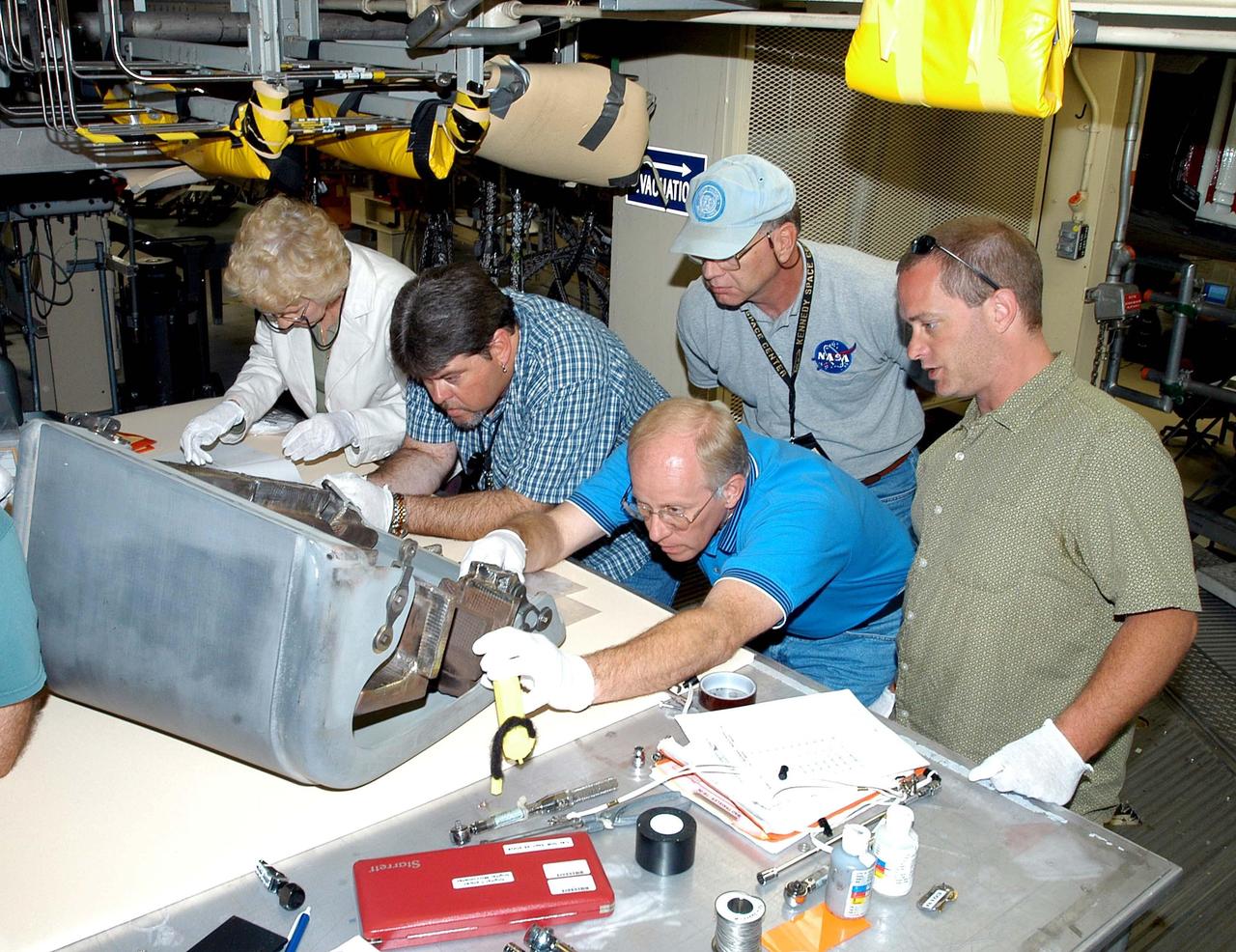 KENNEDY SPACE CENTER, FLA. -  In the Orbiter Processing Facility, several workers check out the first Reinforced Carbon-Carbon panel to be installed on the left wing leading edge on Discovery.  Second from right is Danny Wyatt, NASA Quality Assurance specialist; on the left is Dave Fuller, technician; behind Wyatt is John Legere, NASA Quality Assurance specialist.   The RCC panels are mechanically attached to the wing with spars, a series of floating joints to reduce loading on the panels caused by wing deflections. The T-seals between each wing leading edge panel allow for lateral motion and thermal expansion differences between the RCC and the orbiter wing.  Discovery has been named as the orbiter to fly on the first Return to Flight mission, STS-114.