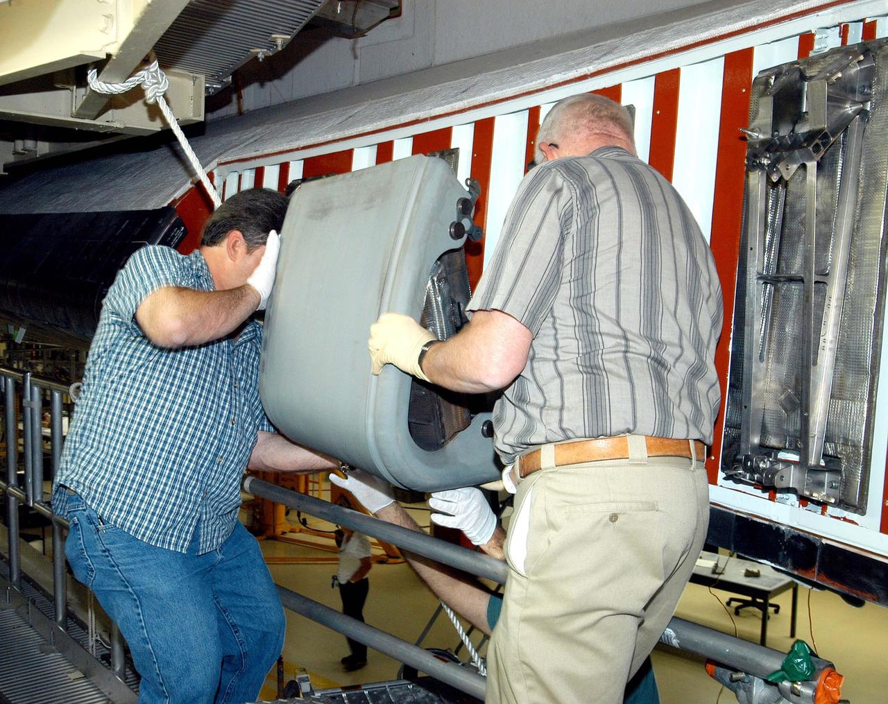 KENNEDY SPACE CENTER, FLA. -  In the Orbiter Processing Facility, United Space Alliance technicians Dave Fuller (left) and Jim Burgess (right) lift the first Reinforced Carbon-Carbon panel toward the left wing leading edge of Discovery for installation. The RCC panels are mechanically attached to the wing with spars, a series of floating joints to reduce loading on the panels caused by wing deflections.  Discovery has been named as the orbiter to fly on the first Return to Flight mission, STS-114.