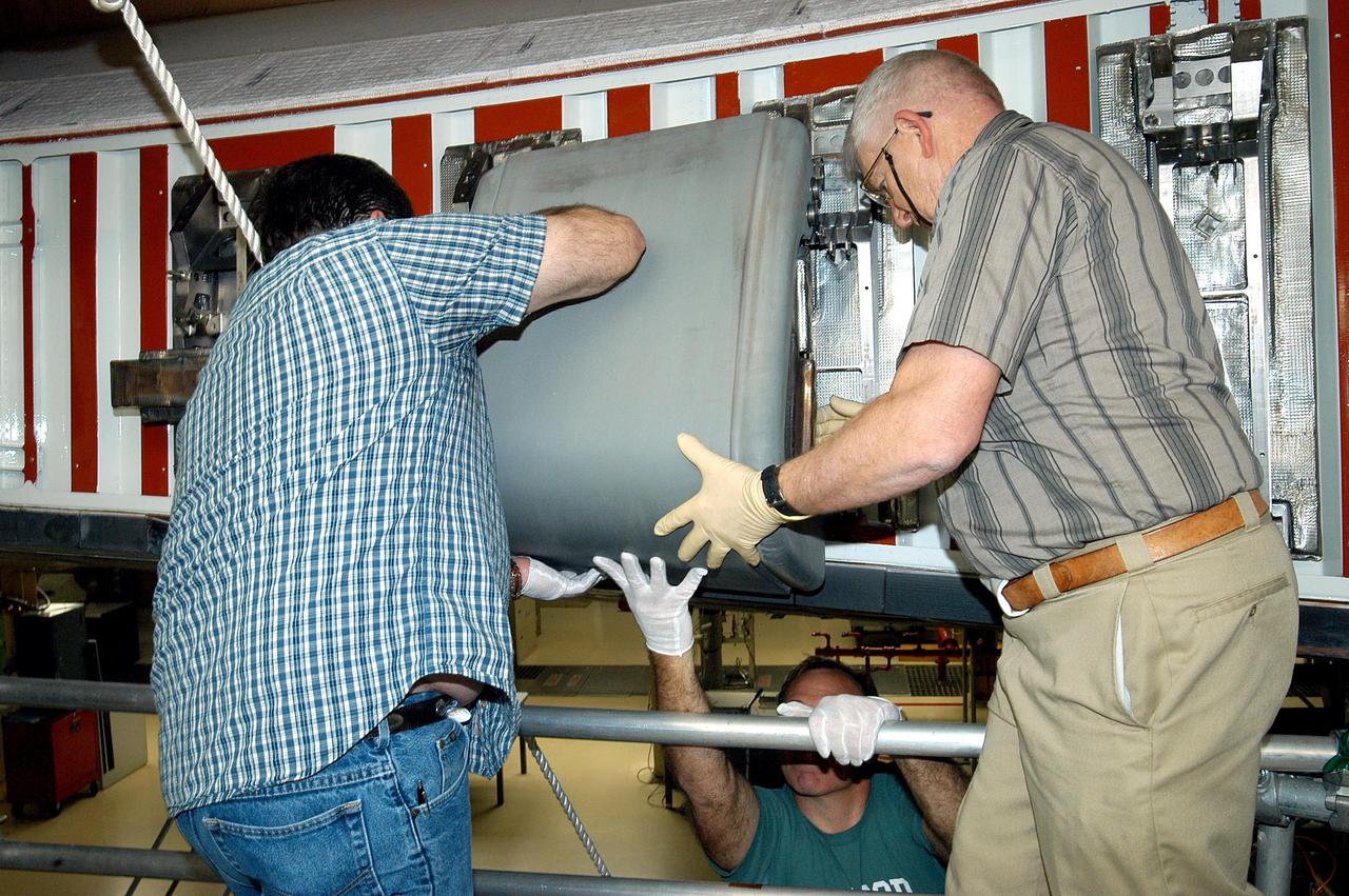 KENNEDY SPACE CENTER, FLA. -  In the Orbiter Processing Facility, United Space Alliance technicians Dave Fuller (left) and Jim Burgess (right) lift into place the first Reinforced Carbon-Carbon panel toward the left wing leading edge of Discovery for installation. The RCC panels are mechanically attached to the wing with spars, a series of floating joints to reduce loading on the panels caused by wing deflections. Discovery has been named as the orbiter to fly on the first Return to Flight mission, STS-114.