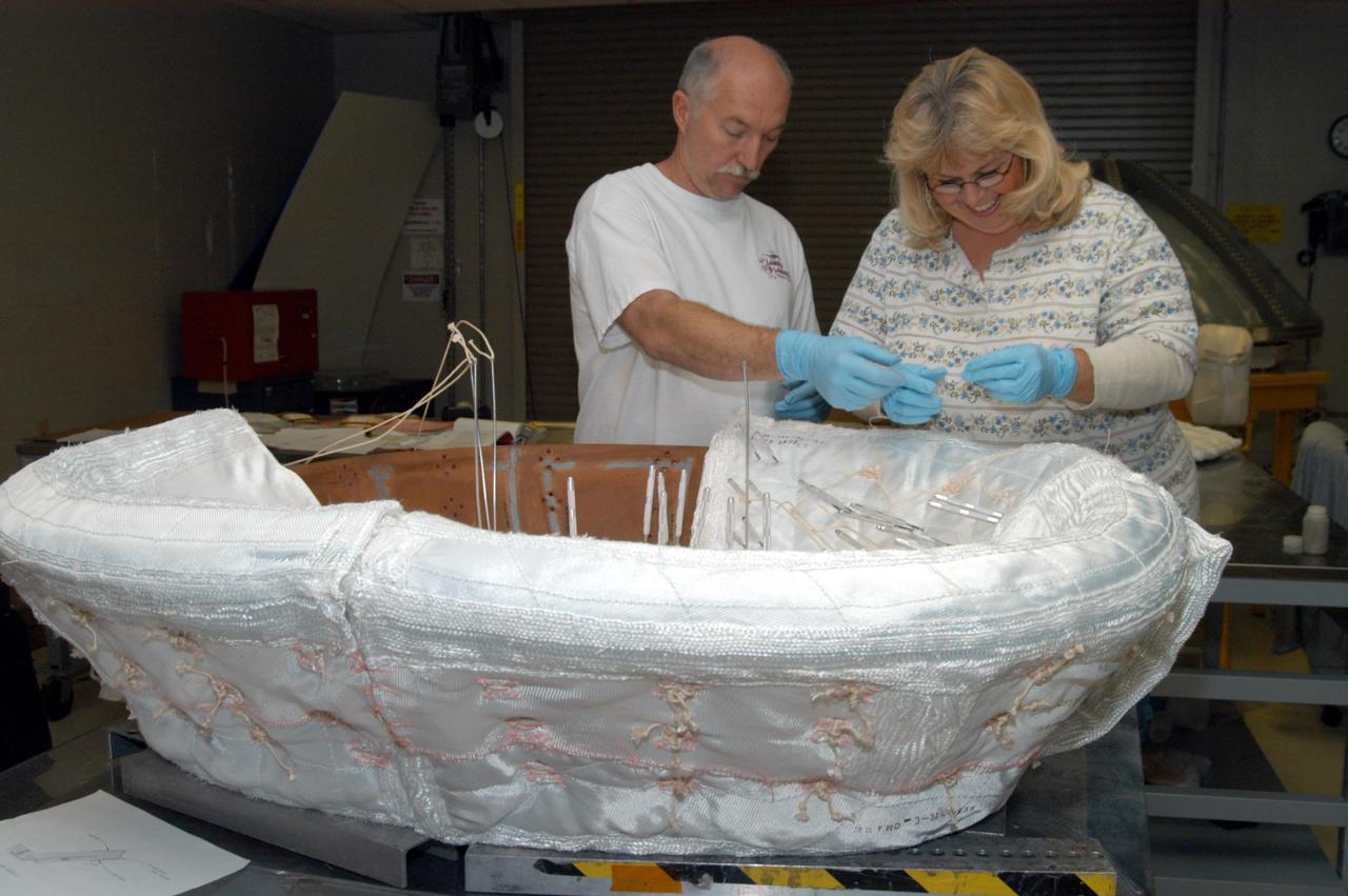 KENNEDY SPACE CENTER, FLA. -- United Space Alliance workers Michael Williams and Ginger Morrison stitch together pieces of insulation blankets inside the ring that fits in the nose cap of Discovery.  The blankets consist of layered, pure silica felt sandwiched between a layer of silica fabric (the hot side) and a layer of S-Glass fabric. The blankets are semi-rigid and can be made as large as 30 inches by 30 inches. The blanket is through-stitched with pure silica thread in a 1-inch grid pattern. After fabrication, the blanket is bonded directly to the vehicle structure and finally coated with a high purity silica coating that improves erosion resistance.
