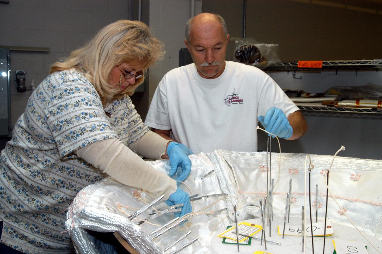 KENNEDY SPACE CENTER, FLA. -- United Space Alliance workers Ginger Morrison and Michael Williams stitch together pieces of insulation blankets inside the ring that fits in the nose cap of Discovery.  The blankets consist of layered, pure silica felt sandwiched between a layer of silica fabric (the hot side) and a layer of S-Glass fabric. The blankets are semi-rigid and can be made as large as 30 inches by 30 inches. The blanket is through-stitched with pure silica thread in a 1-inch grid pattern. After fabrication, the blanket is bonded directly to the vehicle structure and finally coated with a high purity silica coating that improves erosion resistance.
