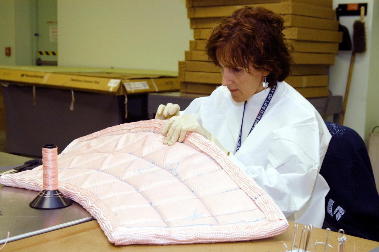 KENNEDY SPACE CENTER, FLA. -- In the Thermal Protection System Facility, Pilar Ryan, with United Space Alliance, stitches a piece of insulation blanket for Atlantis's nose cap.  The blankets consist of layered, pure silica felt sandwiched between a layer of silica fabric (the hot side) and a layer of S-Glass fabric. The blankets are semi-rigid and can be made as large as 30 inches by 30 inches. The blanket is through-stitched with pure silica thread in a 1-inch grid pattern. After fabrication, the blanket is bonded directly to the vehicle structure and finally coated with a high purity silica coating that improves erosion resistance.
