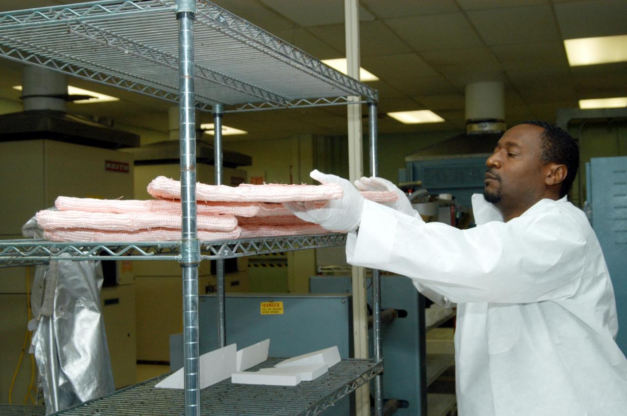 KENNEDY SPACE CENTER, FLA. -- Damon Petty, with United Space Alliance, removes an insulation blanket from a shelf prior to heat cleaning and waterproofing. The blankets fit inside the nose cap of an orbiter. They consist of layered, pure silica felt sandwiched between a layer of silica fabric (the hot side) and a layer of S-Glass fabric. The blanket is through-stitched with pure silica thread in a 1-inch grid pattern. After fabrication, the blanket is bonded directly to the vehicle structure and finally coated with a high purity silica coating that improves erosion resistance. The blankets are semi-rigid and can be made as large as 30 inches by 30 inches.