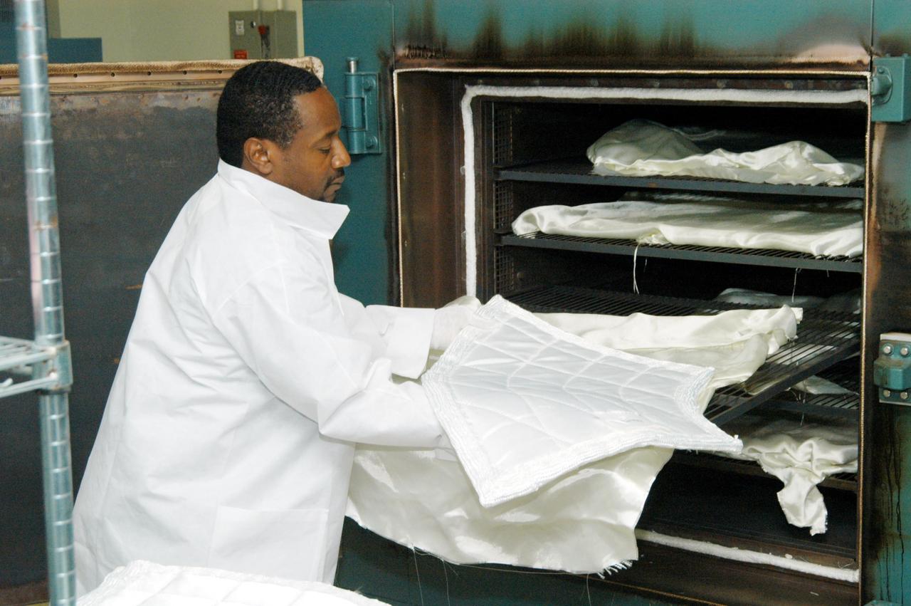 KENNEDY SPACE CENTER, FLA. -- Damon Petty, with United Space Alliance, removes a piece of insulation blanket from an “oven” after heat cleaning. The blankets fit inside the nose cap of an orbiter. They consist of layered, pure silica felt sandwiched between a layer of silica fabric (the hot side) and a layer of S-Glass fabric. The blanket is through-stitched with pure silica thread in a 1-inch grid pattern. After fabrication, the blanket is bonded directly to the vehicle structure and finally coated with a high purity silica coating that improves erosion resistance. The blankets are semi-rigid and can be made as large as 30 inches by 30 inches.