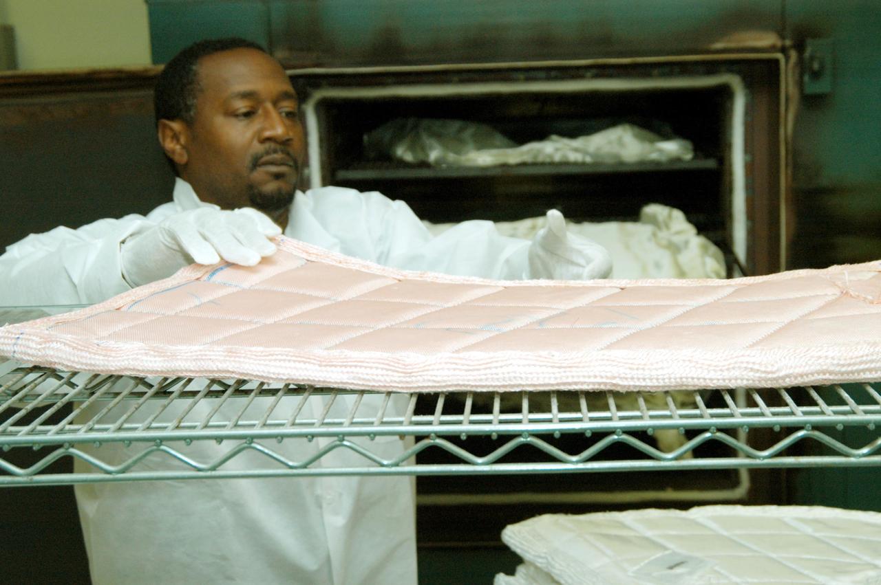 KENNEDY SPACE CENTER, FLA. -- Damon Petty, with United Space Alliance, removes another insulation blanket from a shelf prior to heat cleaning and waterproofing. The blankets fit inside the nose cap of an orbiter. They consist of layered, pure silica felt sandwiched between a layer of silica fabric (the hot side) and a layer of S-Glass fabric. The blanket is through-stitched with pure silica thread in a 1-inch grid pattern. After fabrication, the blanket is bonded directly to the vehicle structure and finally coated with a high purity silica coating that improves erosion resistance. The blankets are semi-rigid and can be made as large as 30 inches by 30 inches.