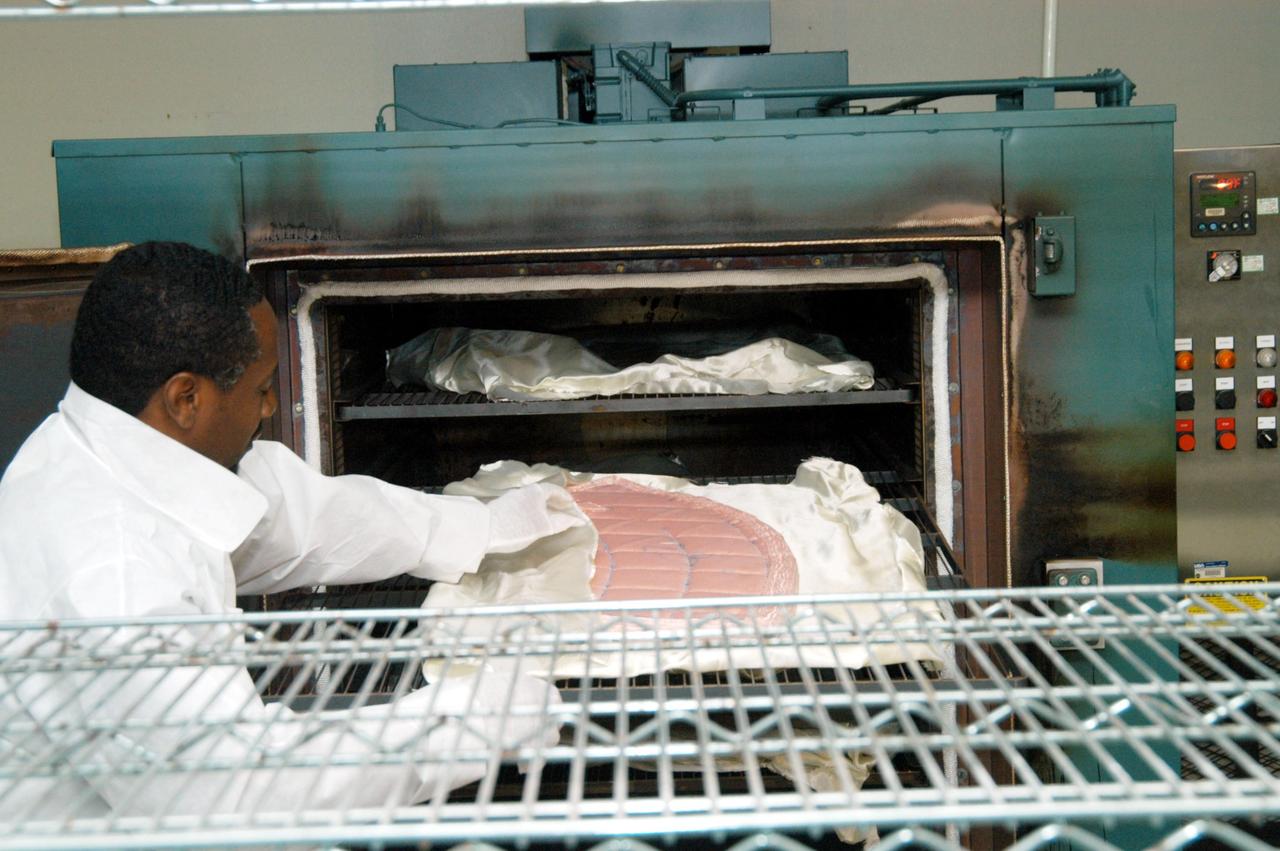 KENNEDY SPACE CENTER, FLA. -- Damon Petty, with United Space Alliance, covers another insulation blanket in the “oven” prior to heat cleaning. The blankets fit inside the nose cap of an orbiter. They consist of layered, pure silica felt sandwiched between a layer of silica fabric (the hot side) and a layer of S-Glass fabric. The blanket is through-stitched with pure silica thread in a 1-inch grid pattern. After fabrication, the blanket is bonded directly to the vehicle structure and finally coated with a high purity silica coating that improves erosion resistance. The blankets are semi-rigid and can be made as large as 30 inches by 30 inches.
