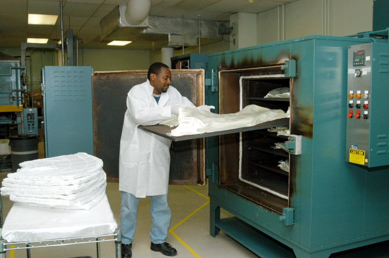 KENNEDY SPACE CENTER, FLA. -- Damon Petty, with United Space Alliance, prepares the cover of another insulation blanket in the “oven” prior to heat cleaning. The blankets fit inside the nose cap of an orbiter. They consist of layered, pure silica felt sandwiched between a layer of silica fabric (the hot side) and a layer of S-Glass fabric. The blanket is through-stitched with pure silica thread in a 1-inch grid pattern. After fabrication, the blanket is bonded directly to the vehicle structure and finally coated with a high purity silica coating that improves erosion resistance. The blankets are semi-rigid and can be made as large as 30 inches by 30 inches.