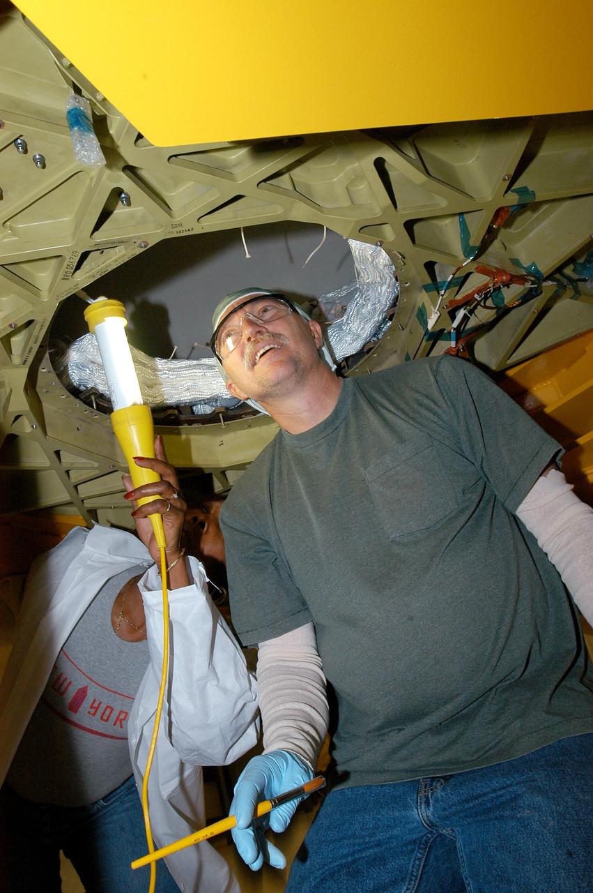 KENNEDY SPACE CENTER, FLA. -- United Space Alliance technician Mike Williams peers into the underside of the Discovery’s nose cap. He is part of the team installing the thermal blanket insulation in the nose cap. The work is being done in a low bay area outside the Orbiter Processing Facility. Discovery is the orbiter named as the vehicle for Return to Flight with mission STS-114.