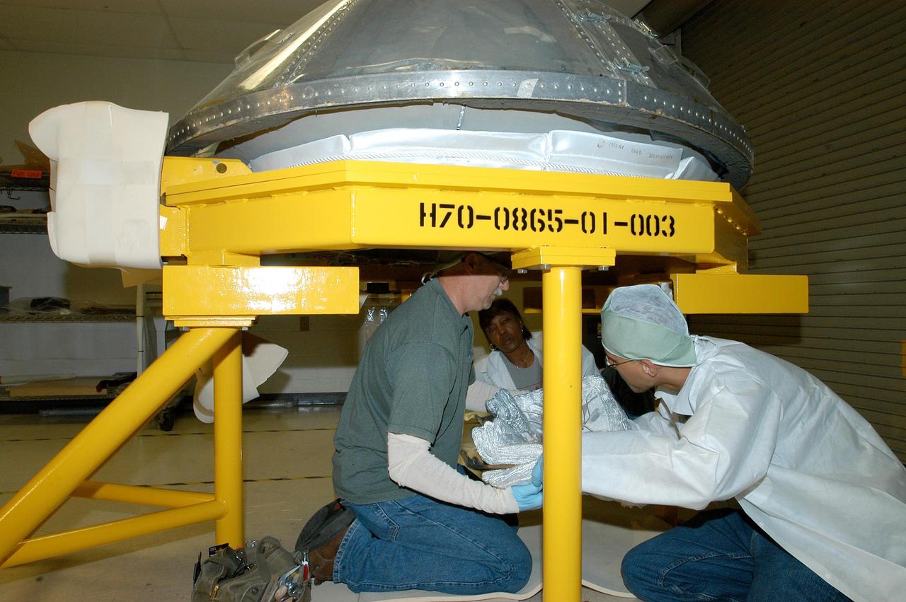 KENNEDY SPACE CENTER, FLA. -- United Space Alliance (USA) technicians Mike Williams (left), Pearl Richardson (center) and R. Justin Hopmann get ready to lift the thermal blanket insulation into Discovery’s nose cap, which is under a protective cover and seated above on a work stand.  The work is being done in a low bay area outside the Orbiter Processing Facility.  Discovery is the orbiter named as the vehicle for Return to Flight with mission STS-114.