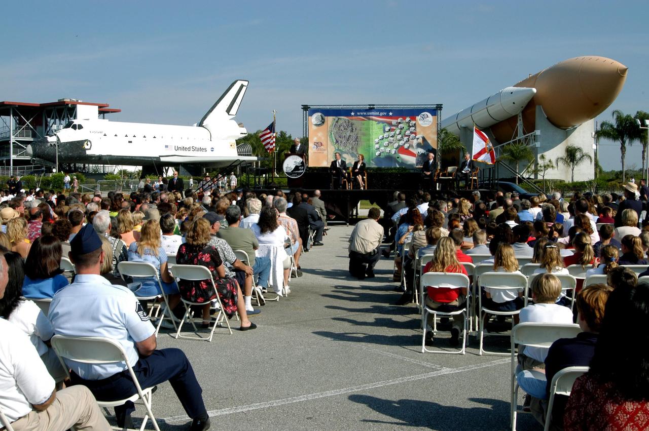 KENNEDY SPACE CENTER, FLA. -- On the stage framed between the orbiter mockup and SRB-external tank exhibit at the KSC Visitor Complex, NASA Administrator Sean O’Keefe comments on the design of the new Florida quarter during the launch ceremony.  Sharing the stage with him are Florida Gov. Jeb Bush, U.S. Mint Director Henrietta Holsman Fore, Deputy Secretary of the Treasury Samuel W. Bodman and Center Director Jim Kennedy, who emceed.  The quarter celebrates Florida as a destination for explorers in the past, a launch site for future explorers into space and an inviting place for visitors today.