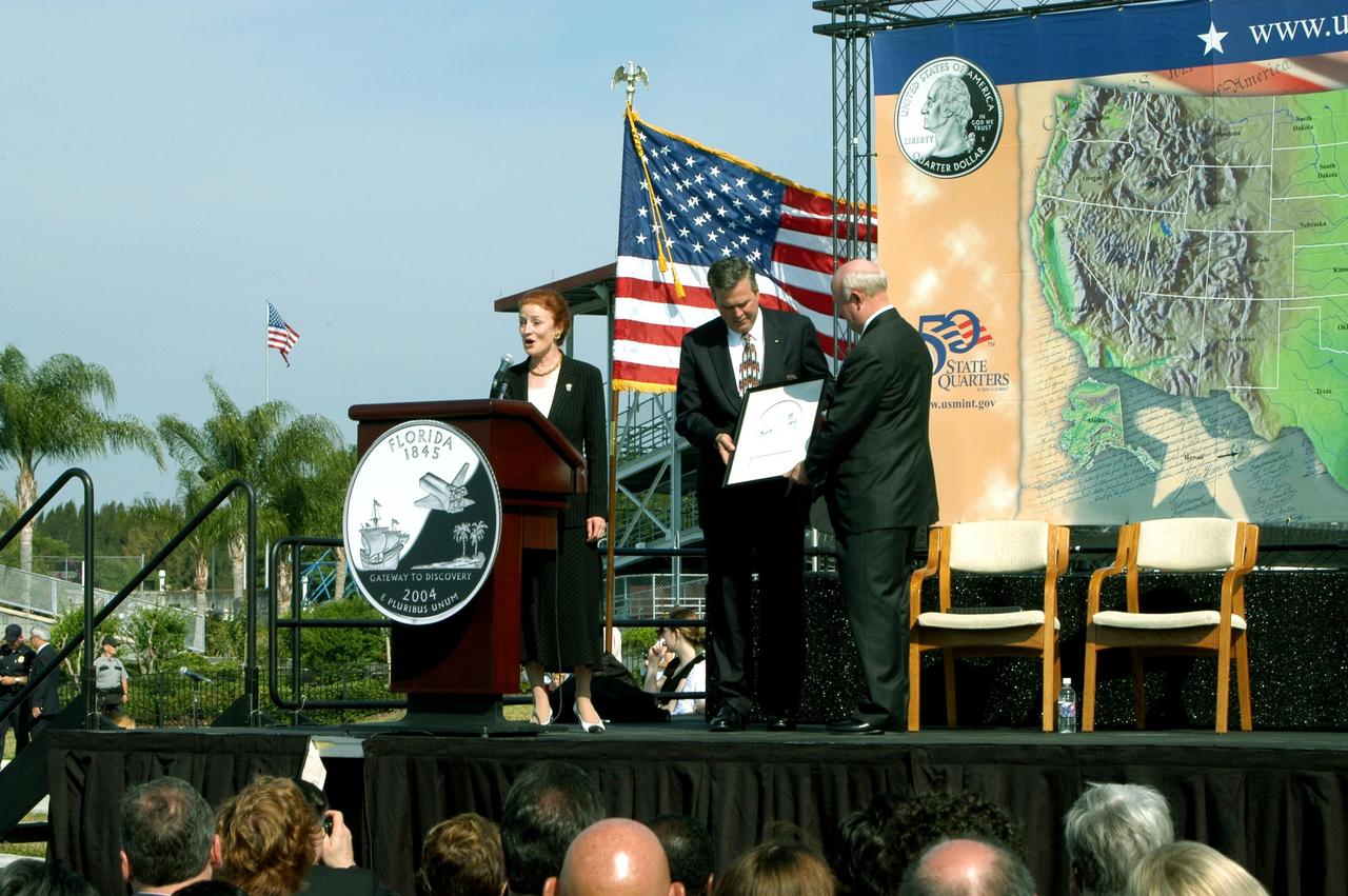 KENNEDY SPACE CENTER, FLA. -- U.S. Mint Director Henrietta Holsman Fore presents the new Florida quarter at its unveiling ceremony, held at the KSC Visitor Complex. Florida Gov. Jeb Bush and Deputy Secretary of the Treasury Samuel W. Bodman hold a framed representation of the quarter design. The quarter celebrates Florida as the gateway to discovery -- a destination for explorers in the past, a launch site for space explorers of the future, and an inviting place for visitors today.