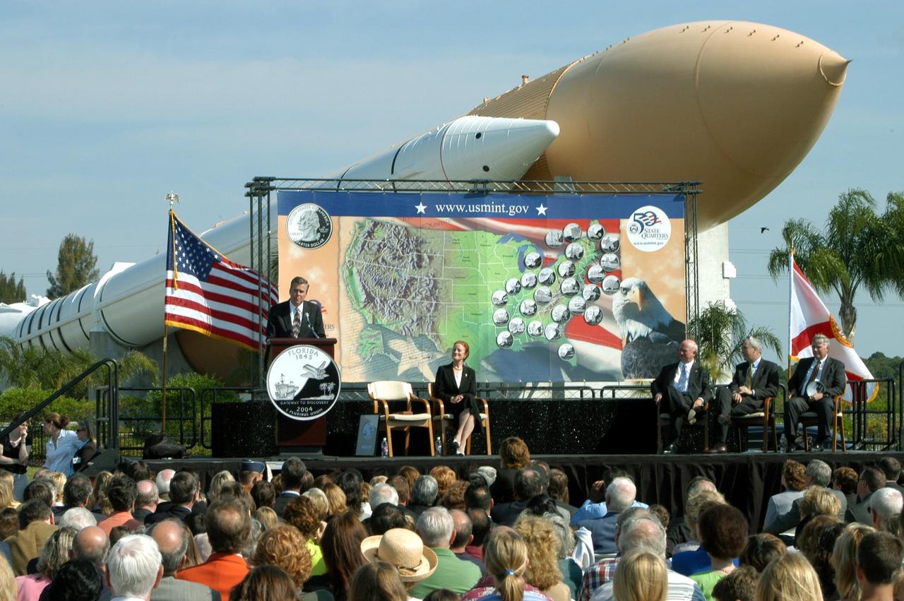 KENNEDY SPACE CENTER, FLA. -- Florida Gov. Jeb Bush addresses the audience at a ceremony to launch the new Florida quarter, held at the KSC Visitor Complex. The Solid Rocket Booster/External Tank exhibit towers over a map of the United States set up on stage, illustrating the state quarters issued to date. Sharing the stage with him are, from left, U.S. Mint Director Henrietta Holsman Fore, Deputy Secretary of the Treasury Samuel W. Bodman, NASA Administrator Sean O'Keefe, and KSC Director James W. Kennedy. The quarter celebrates Florida as the gateway to discovery -- a destination for explorers in the past, a launch site for space explorers of the future, and an inviting place for visitors today.