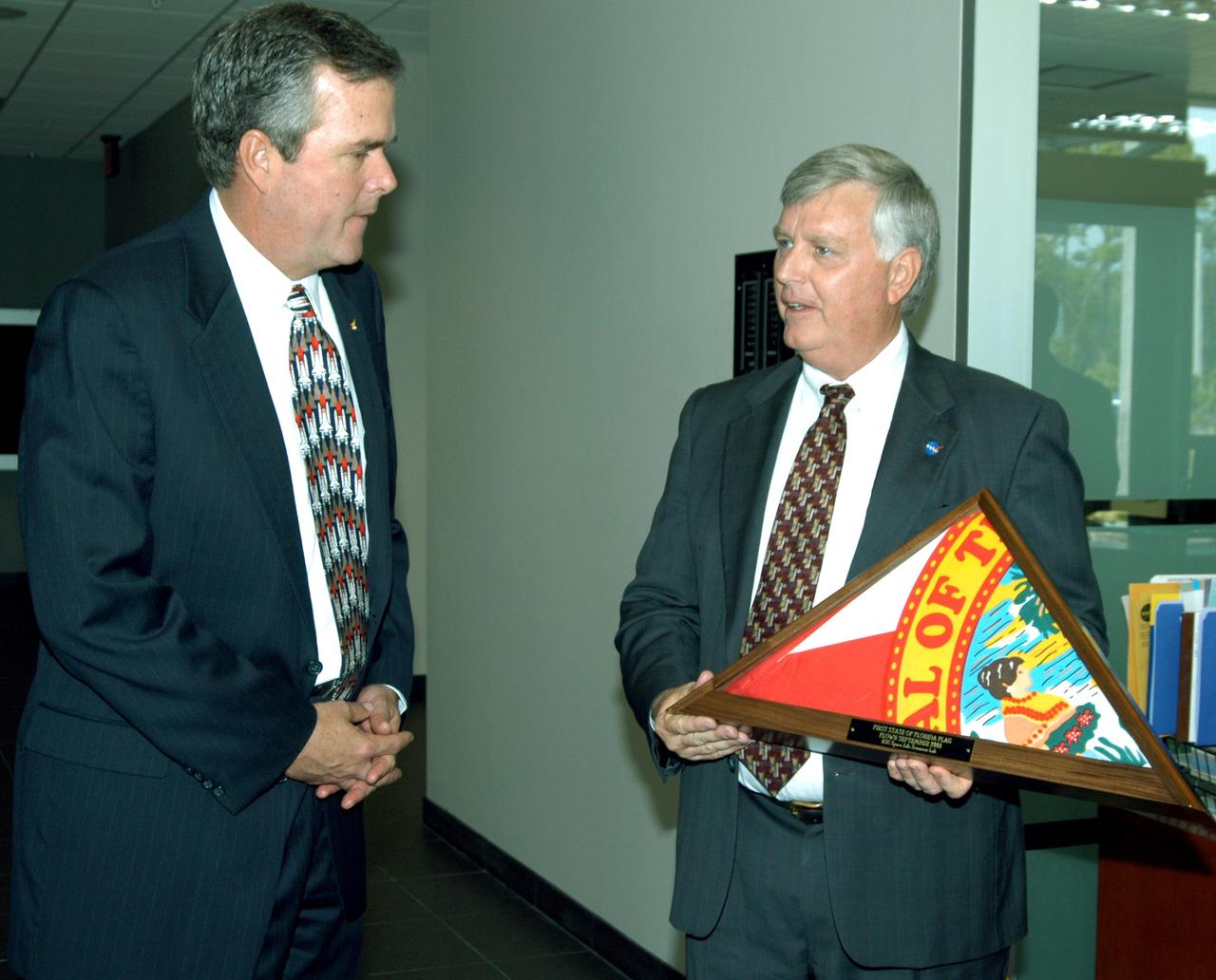 KENNEDY SPACE CENTER, FLA. -- Center Director Jim Kennedy presents a Florida flag to Florida Gov. Jeb Bush.  The flag was flown during construction of the Space Life Sciences Lab through dedication of the Lab. The presentation was during a tour of the Lab following the launching ceremony at the KSC Visitor Complex for the new Florida quarter issued by the U.S. Mint.  The ceremony was emceed by Center Director Jim Kennedy and included remarks by NASA Administrator Sean O’Keefe, Bush, U.S. Mint Director Henrietta Holsman Fore and Deputy Secretary of the Treasury Samuel W. Bodman. The new lab is a state-of-the-art facility built for ISS biotechnology research. It was developed as a partnership between NASA-KSC and the State of Florida.