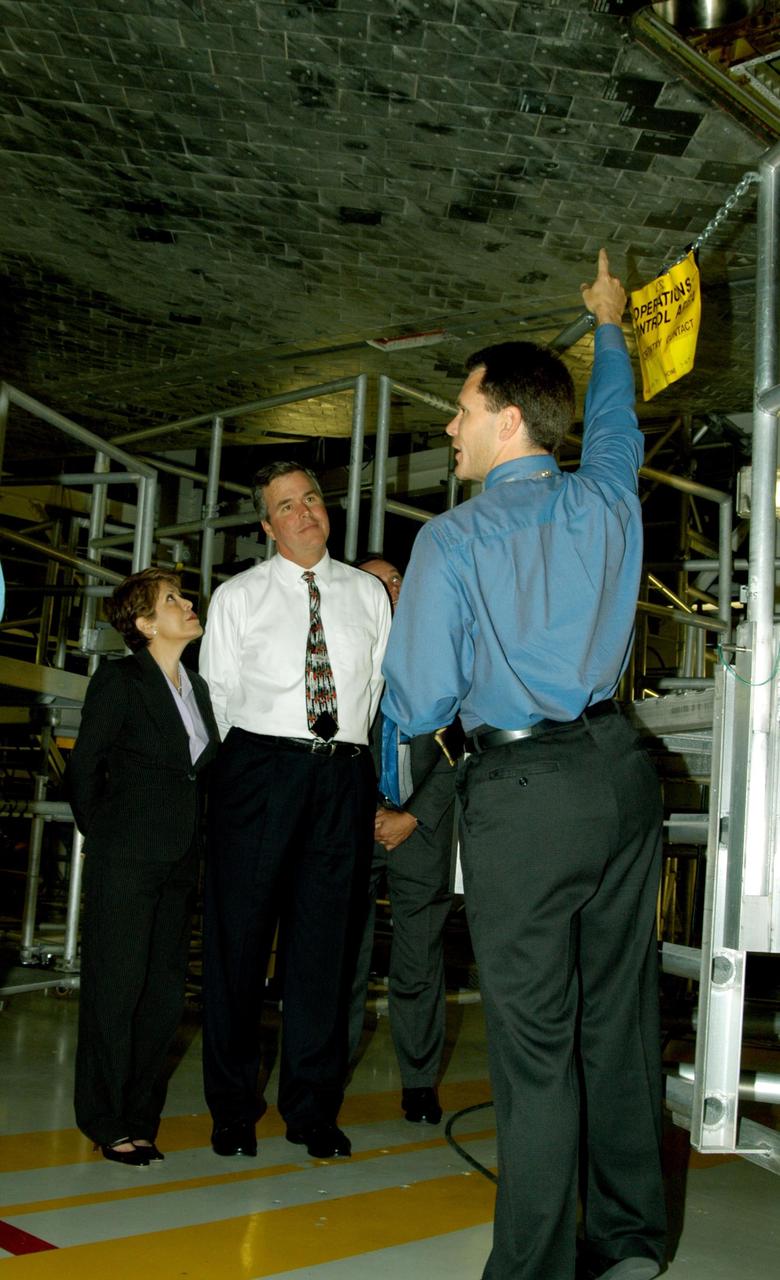 KENNEDY SPACE CENTER, FLA. -- On a tour of the Orbiter Processing Facility, Florida Gov. Jeb Bush (center) and his wife, Columba (left), listen to NASA Vehicle Manager Scott Thurston talk about the orbiter Atlantis overhead.  The tour followed the launching ceremony at the KSC Visitor Complex for the new Florida quarter issued by the U.S. Mint. The ceremony was emceed by Center Director Jim Kennedy and included remarks by NASA Administrator Sean O’Keefe, Bush, U.S. Mint Director Henrietta Holsman Fore and Deputy Secretary of the Treasury Samuel W. Bodman.