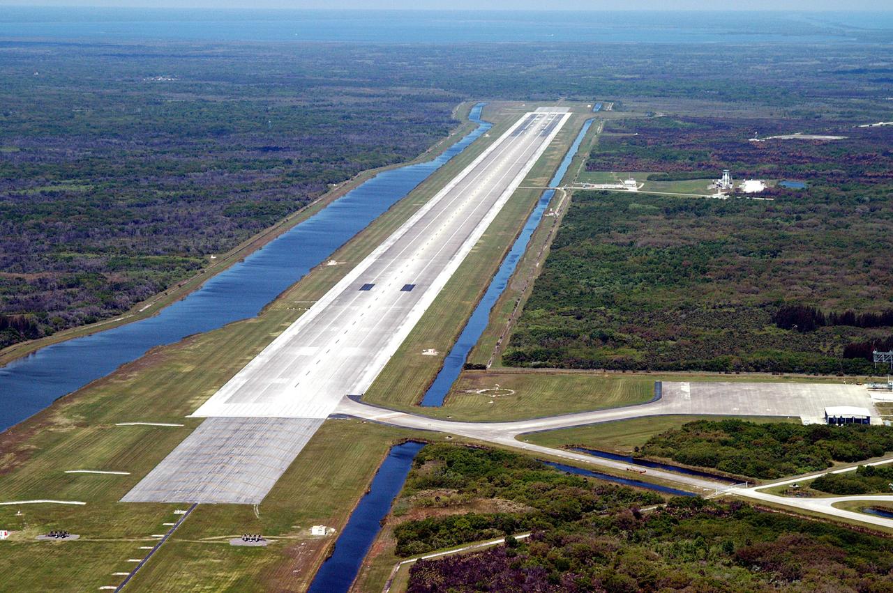 KENNEDY SPACE CENTER, FLA. - This aerial photo of the runway at the KSC Shuttle Landing Facility looks north.  Longer and wider than most commercial runways, it is 15,000 feet long, with 1,000-foot paved overruns on each end, and 300 feet wide, with 50-foot asphalt shoulders.  The runway is used by military and civilian cargo carriers, astronauts’ T-38 trainers, Shuttle Training Aircraft and helicopters, as well as the Space Shuttle.  On the lower right is the parking apron with the orbiter mate/demate tower and the tow-way stretching from the runway to the lower right.  Farther north is a grassy area where the new control tower is located.