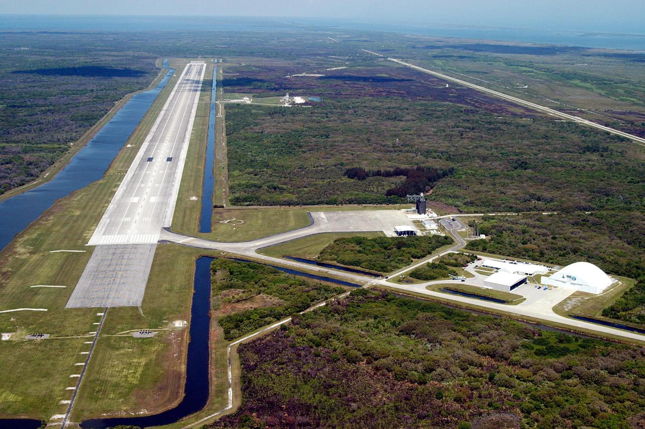 KENNEDY SPACE CENTER, FLA. - This aerial photo of the runway at the KSC Shuttle Landing Facility looks northeast.  Longer and wider than most commercial runways, it is 15,000 feet long, with 1,000-foot paved overruns on each end, and 300 feet wide, with 50-foot asphalt shoulders.  The runway is used by military and civilian cargo carriers, astronauts’ T-38 trainers, Shuttle Training Aircraft and helicopters, as well as the Space Shuttle.  At center right is the parking apron with the orbiter mate/demate tower.  The tow-way stretches from the runway to the right, passing the hangar and storage facilities.  A grassy area next to the mid-point of the runway is where the new control tower is located.