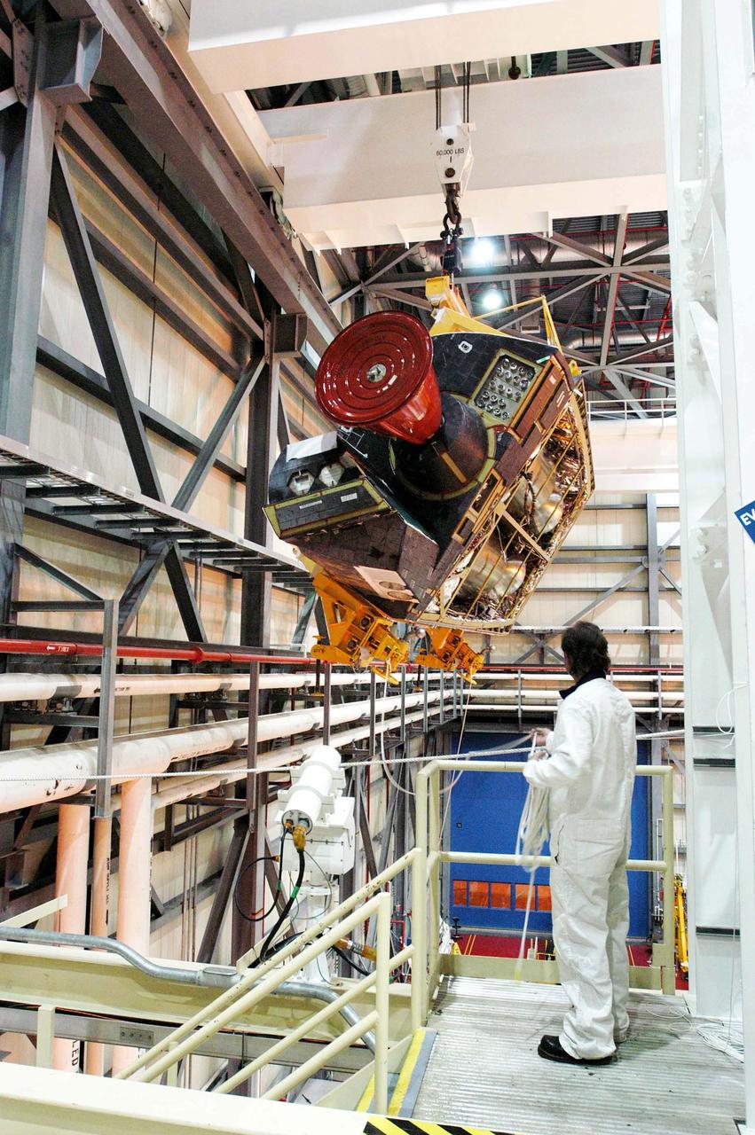 KENNEDY SPACE CENTER, FLA. - In the Orbiter Processing Facility, a worker on an upper level watches as the left-hand Orbital Maneuvering System (OMS) pod is lifted high to maneuver it toward the orbiter Discovery for installation. The Orbital Maneuvering System provides the thrust for orbit insertion, orbit circularization, orbit transfer, rendezvous, deorbit, abort to orbit and abort once around. It can provide up to 1,000 pounds of propellant to the aft reaction control system. Each pod contains one OMS engine and the hardware needed to pressurize, store and distribute the propellants to perform the velocity maneuvers.