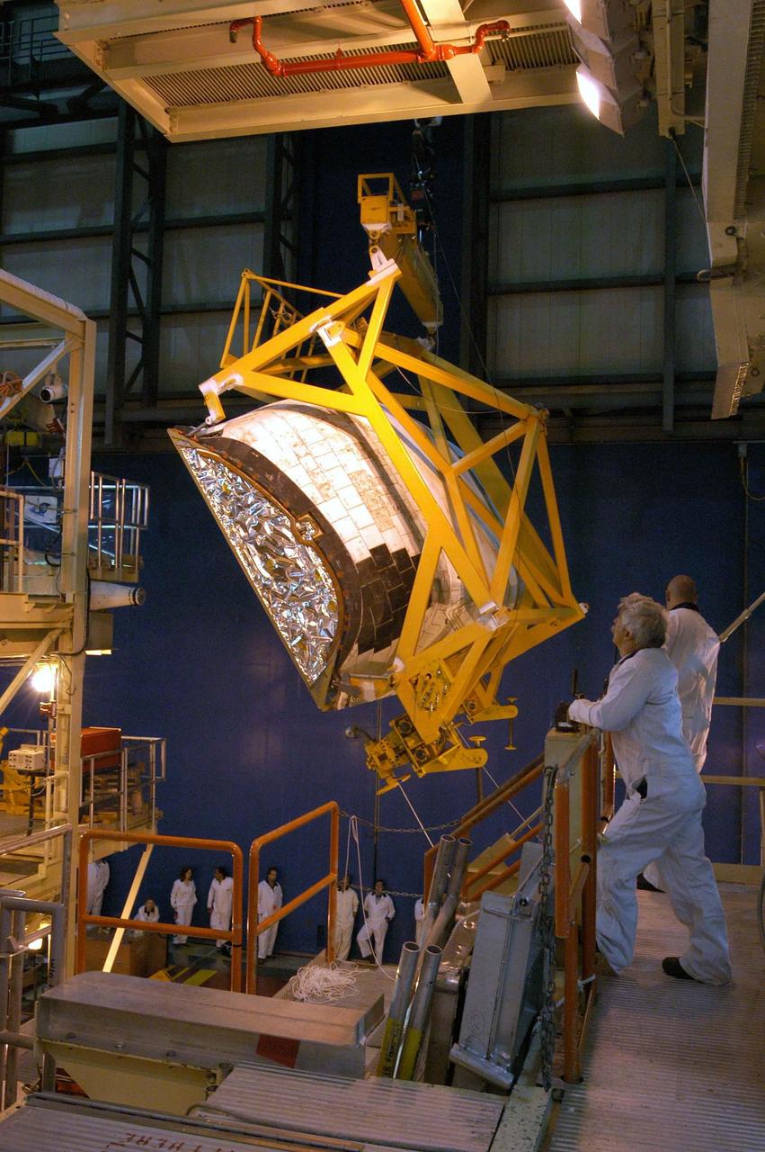 KENNEDY SPACE CENTER, FLA. - In the Orbiter Processing Facility, workers on an upper level watch as the left-hand Orbital Maneuvering System (OMS) pod is lifted high to maneuver it toward the orbiter Discovery for installation. The Orbital Maneuvering System provides the thrust for orbit insertion, orbit circularization, orbit transfer, rendezvous, deorbit, abort to orbit and abort once around. It can provide up to 1,000 pounds of propellant to the aft reaction control system. Each pod contains one OMS engine and the hardware needed to pressurize, store and distribute the propellants to perform the velocity maneuvers.