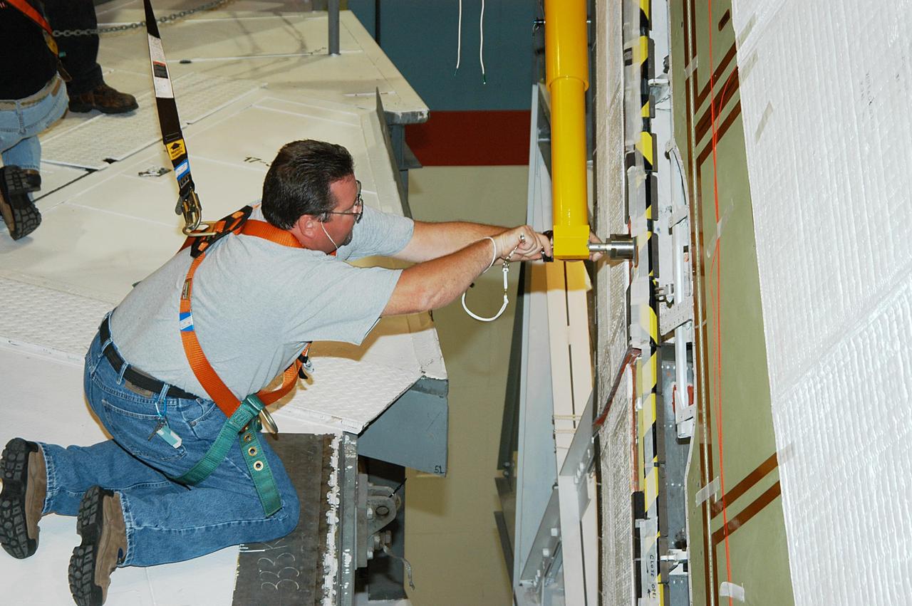 KENNEDY SPACE CENTER, FLA. -- In the Orbiter Processing Facility, a worker tightens a fitting on the device being used to remove the Rudder Speed Brake panel on the vertical tail of the orbiter Atlantis. The Rudder Speed Brake is being removed for inspection and maintenance prior to Return to Flight. The vertical tail consists of a structural fin surface made of aluminum, the Rudder Speed Brake surface, a tip and a lower trailing edge. The rudder splits into two halves to serve as a speed brake. The vertical tail and Rudder Speed Brake are covered with a reusable thermal protection system. The Rudder Speed Brake is used to guide and slow the Shuttle as it comes in for a landing.