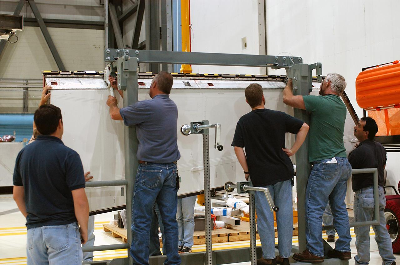 KENNEDY SPACE CENTER, FLA. -- In the Orbiter Processing Facility, workers attach Atlantis’ Rudder Speed Brake panel to a stand after removing the panel from the vertical tail. The Rudder Speed Brake is being removed for inspection and maintenance prior to Return to Flight. The vertical tail consists of a structural fin surface made of aluminum, the Rudder Speed Brake surface, a tip and a lower trailing edge. The rudder splits into two halves to serve as a speed brake. The vertical tail and Rudder Speed Brake are covered with a reusable thermal protection system. The Rudder Speed Brake is used to guide and slow the Shuttle as it comes in for a landing.