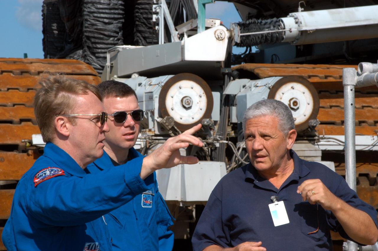 KENNEDY SPACE CENTER, FLA. -- STS-114 Mission Specialist Andrew Thomas (left) talks to NASA Systems Engineer Robert Rokobauer (right) about the Crawler-Transporters.  At center is Pilot James Kelly. Behind them is one of the 5.5-million-pound crawlers. The 10-foot-high track, one of two, contains 278 “shoes,” weighing 2,200 pounds each.  The crawlers are guided by four trucks, one on each corner.  The crawlers had recent modifications to the cab and muffler system.  The STS-114 mission is Logistics Flight 1, which is scheduled to deliver supplies and equipment plus the external stowage platform to the International Space Station.