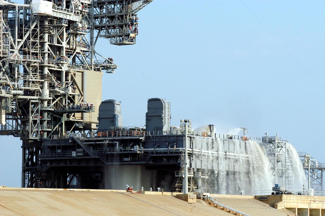 KENNEDY SPACE CENTER, FLA. -- For the fourth time in Space Shuttle Program history, 350,000 gallons of water are being released on a Mobile Launcher Platform (MLP) at Launch Pad 39A during a water sound suppression test. Because of the unusual event, media and workers watch from nearby vantage points on the Fixed Service Structure (left). This test is being conducted following the replacement of the six main system valves, which had been in place since the beginning of the Shuttle Program and had reached the end of their service life. Also, the hydraulic portion of the valve actuators has been redesigned and simplified to reduce maintenance costs. The sound suppression water system is installed on the launch pads to protect the orbiter and its payloads from damage by acoustical energy reflected from the MLP during launch. The system includes an elevated water tank with a capacity of 300,000 gallons. The tank is 290 feet high and stands on the northeast side of the Pad. The water is released just before the ignition of the orbiter's three main engines and twin solid rocket boosters, and flows through parallel 7-foot-diameter pipes to the Pad area.