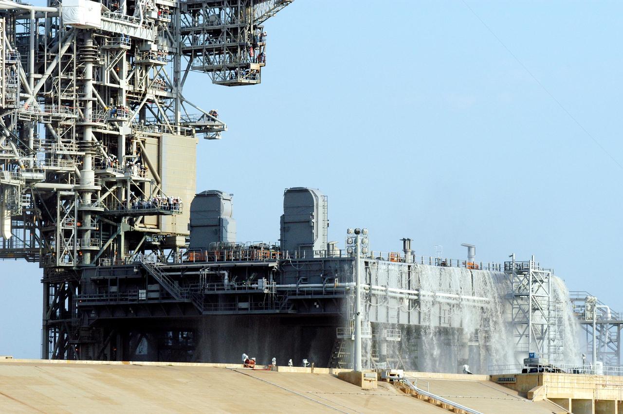 KENNEDY SPACE CENTER, FLA. -- For the fourth time in Space Shuttle Program history, 350,000 gallons of water are being released on a Mobile Launcher Platform (MLP) at Launch Pad 39A during a water sound suppression test. Because of the unusual event, media and workers watch from nearby vantage points on the Fixed Service Structure (left). This test is being conducted following the replacement of the six main system valves, which had been in place since the beginning of the Shuttle Program and had reached the end of their service life. Also, the hydraulic portion of the valve actuators has been redesigned and simplified to reduce maintenance costs. The sound suppression water system is installed on the launch pads to protect the orbiter and its payloads from damage by acoustical energy reflected from the MLP during launch. The system includes an elevated water tank with a capacity of 300,000 gallons. The tank is 290 feet high and stands on the northeast side of the Pad. The water is released just before the ignition of the orbiter's three main engines and twin solid rocket boosters, and flows through parallel 7-foot-diameter pipes to the Pad area.