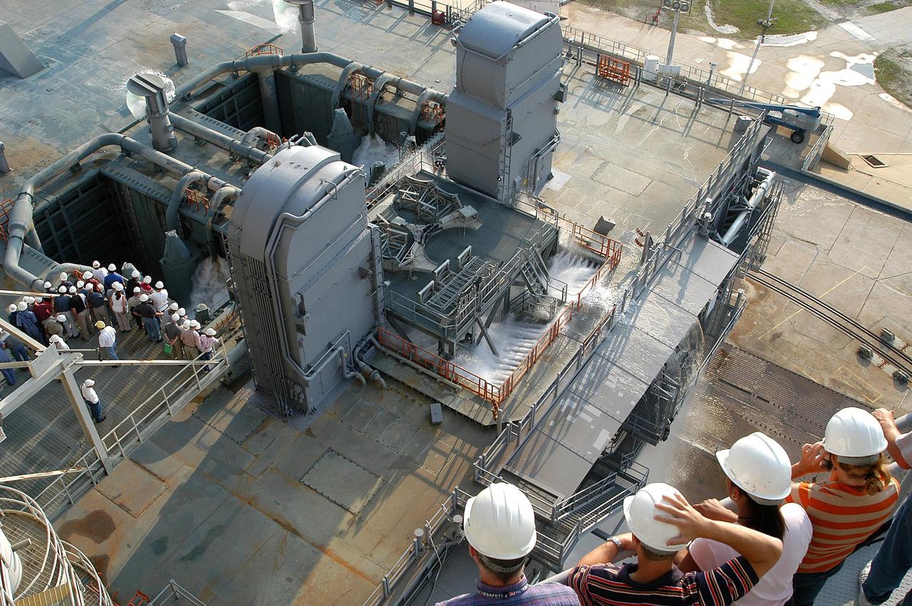 KENNEDY SPACE CENTER, FLA. -- From vantage points on the Fixed Service Structure (bottom right and left) on Launch Pad 39A, workers and the media look down upon the Mobile Launcher Platform (MLP) at the start of a water sound suppression test. This test is being conducted following the replacement of the six main system valves, which had been in place since the beginning of the Shuttle Program and had reached the end of their service life. Also, the hydraulic portion of the valve actuators has been redesigned and simplified to reduce maintenance costs. The sound suppression water system is installed on the launch pads to protect the orbiter and its payloads from damage by acoustical energy reflected from the MLP during launch. The system includes an elevated water tank with a capacity of 300,000 gallons. The tank is 290 feet high and stands on the northeast side of the Pad. The water is released just before the ignition of the orbiter's three main engines and twin solid rocket boosters, and flows through parallel 7-foot-diameter pipes to the Pad area.