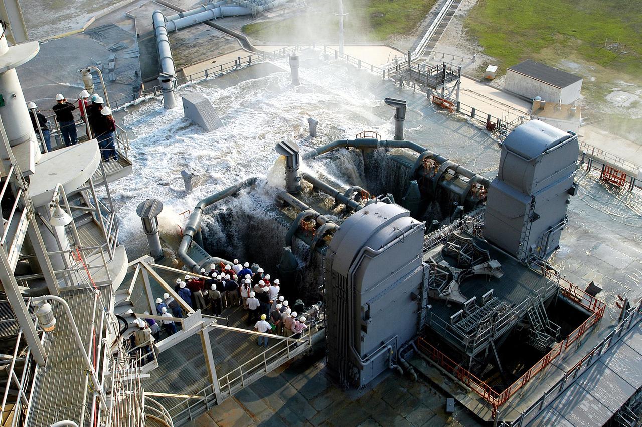 KENNEDY SPACE CENTER, FLA. -- Water recedes from the Mobile Launcher Platform (MLP) on Launch Pad 39A after the water sound suppression test. Workers and the media (left) were on hand to witness the rare event. This test was conducted following the replacement of the six main system valves, which had been in place since the beginning of the Shuttle Program and had reached the end of their service life. Also, the hydraulic portion of the valve actuators has been redesigned and simplified to reduce maintenance costs. The sound suppression water system is installed on the launch pads to protect the orbiter and its payloads from damage by acoustical energy reflected from the MLP during launch. The system includes an elevated water tank with a capacity of 300,000 gallons. The tank is 290 feet high and stands on the northeast side of the Pad. The water is released just before the ignition of the orbiter's three main engines and twin solid rocket boosters, and flows through parallel 7-foot-diameter pipes to the Pad area.