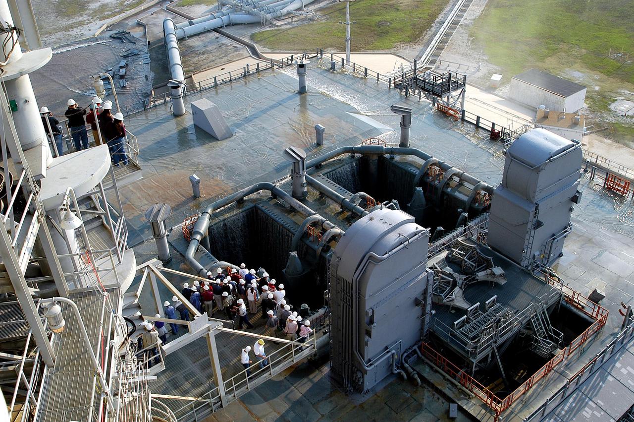 KENNEDY SPACE CENTER, FLA. -- Some water remains on the surface of the Mobile Launcher Platform (MLP) on Launch Pad 39A after a water sound suppression test. Workers and the media (left) were on hand to witness the rare event. This test was conducted following the replacement of the six main system valves, which had been in place since the beginning of the Shuttle Program and had reached the end of their service life. Also, the hydraulic portion of the valve actuators has been redesigned and simplified to reduce maintenance costs. The sound suppression water system is installed on the launch pads to protect the orbiter and its payloads from damage by acoustical energy reflected from the MLP during launch. The system includes an elevated water tank with a capacity of 300,000 gallons. The tank is 290 feet high and stands on the northeast side of the Pad. The water is released just before the ignition of the orbiter's three main engines and twin solid rocket boosters, and flows through parallel 7-foot-diameter pipes to the Pad area.