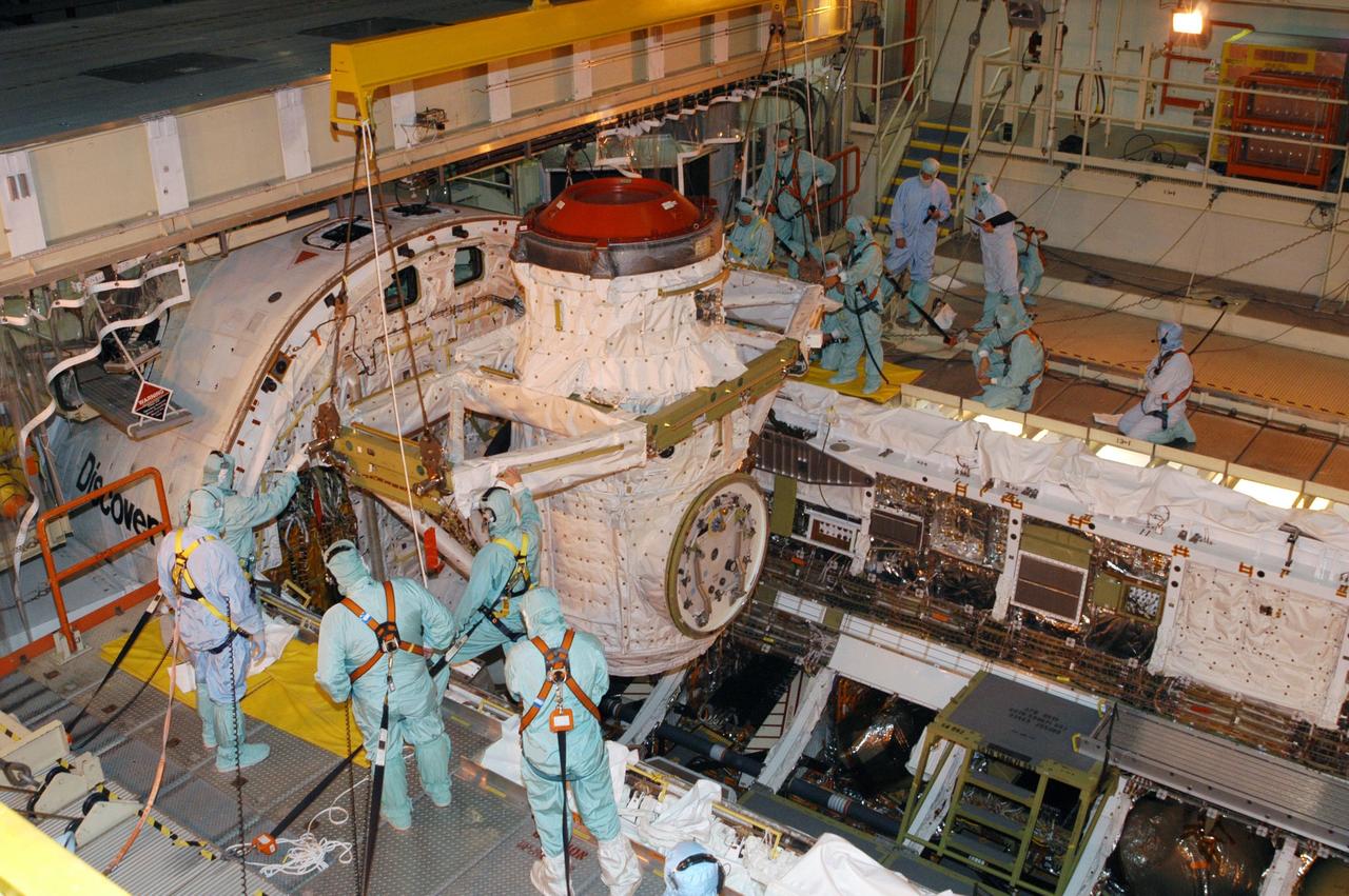 KENNEDY SPACE CENTER, FLA. -- Technicians in the Orbiter Processing Facility help guide Discovery’s airlock as a crane lowers it into the orbiter’s payload bay for installation.  The airlock is sized to accommodate two fully suited flight crew members simultaneously.  Support functions include airlock depressurization and repressurization, extravehicular activity equipment recharge, liquid-cooled garment water cooling, EVA equipment checkout, and communications.  Discovery is designated as the Return to Flight vehicle for mission STS-114, no earlier than March 2005.  STS-114 mission is Logistics Flight 1, which is scheduled to deliver supplies and equipment plus the external stowage platform to the International Space Station.