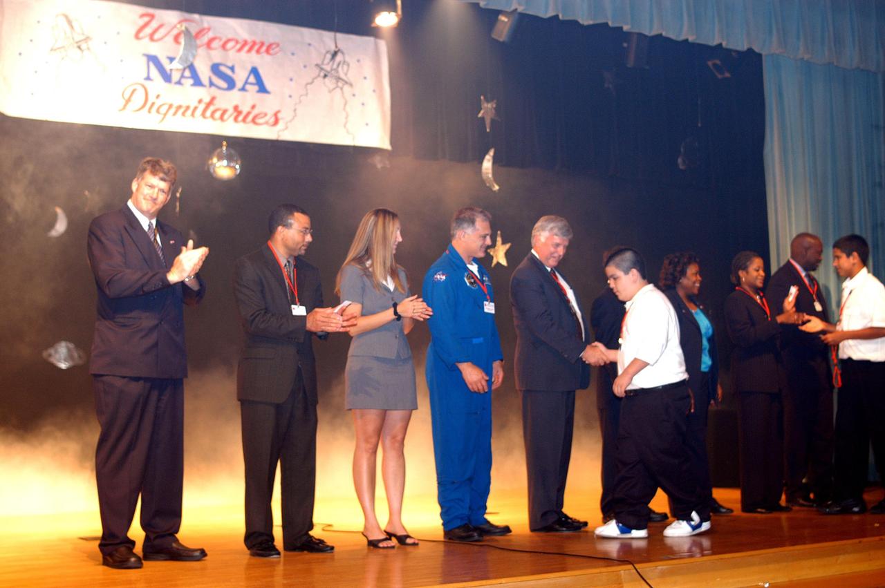 KENNEDY SPACE CENTER, FLA. -- During a visit to Howard A. Doolin Middle School, Miami, Fla., Center Director Jim Kennedy (shaking hands, center) and other NASA and KSC representatives are greeted by students on stage. With Kennedy on stage are (left to right), Jim Gerard, Aerospace Education Services Program (AESP) representative; Steve Lewis, assistant to Kennedy; Amber Marek, with KSC External Relations; David Wolf, astronaut; Kennedy; Les Gold, AESP representative; Burdette Brown; and Patricia Leonard and Clarence Bostic, Education Programs and University Research Division. Doolin Middle School is one of 100 to take part in the NASA Explorer Schools program. Kennedy is talking with students, the next generation of explorers, about our destiny as explorers, NASA’s stepping stone approach to exploring Earth, the Moon, Mars and beyond, how space impacts our lives, and how people and machines rely on each other in space.