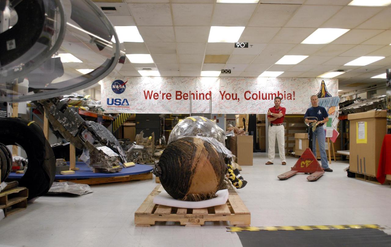KENNEDY SPACE CENTER, FLA.  -  In the Vehicle Assembly Building (VAB), Scott Thurston (red shirt) stands by while a United Space Alliance worker (blue shirt) gets ready to start moving pieces of Columbia debris, such as the PRSD tank in front, for transfer to a shipping facility and delivery to The Aerospace Corporation in El Segundo, Calif.  Thurston is the Columbia debris coordinator.  The pieces have been released for loan to the non-governmental agency for testing and research.   The Aerospace Corporation requested and will receive graphite/epoxy honeycomb skins from an Orbital Maneuvering System pod, Main Propulsion System Helium tanks, a Reaction Control System Helium tank and a Power Reactant Storage Distribution system tank. The company will use the parts to study re-entry effects on composite materials. NASA notified the Columbia crew’s families about the loan before releasing the items for study.  Researchers believe the testing will show how materials are expected to respond to various heating and loads' environments. The findings will help calibrate tools and models used to predict hazards to people and property from reentering hardware. The Aerospace Corporation will have the debris for one year to perform analyses to estimate maximum temperatures during reentry based upon the geometry and mass of the recovered composite.  Columbia’s debris is stored in the VAB.