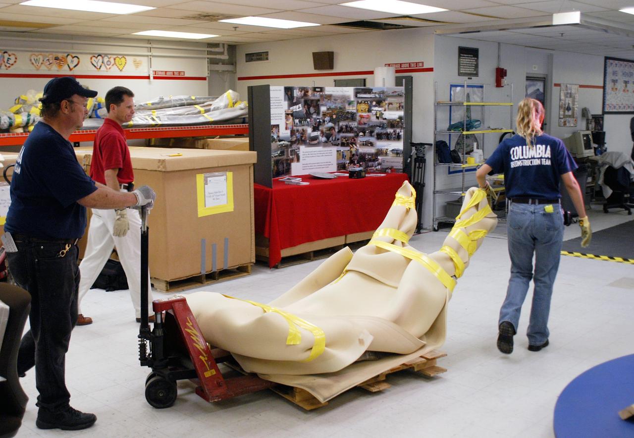 KENNEDY SPACE CENTER, FLA.  -  United Space Alliance workers J.C. Harrison (far left) and Amy Mangiacapra guide a wrapped piece of Columbia debris through the Vehicle Assembly Building, where it is stored.  Alongside is NASA’s Scott Thurston, who is the Columbia debris coordinator.  This piece is one of eight being released to The Aerospace Corporation in El Segundo, Calif., for testing and research.  The Aerospace Corporation requested and will receive graphite/epoxy honeycomb skins from an Orbital Maneuvering System pod, Main Propulsion System Helium tanks, a Reaction Control System Helium tank and a Power Reactant Storage Distribution system tank. The company will use the parts to study re-entry effects on composite materials. NASA notified the Columbia crew’s families about the loan before releasing the items for study.  Researchers believe the testing will show how materials are expected to respond to various heating and loads' environments. The findings will help calibrate tools and models used to predict hazards to people and property from reentering hardware. The Aerospace Corporation will have the debris for one year to perform analyses to estimate maximum temperatures during reentry based upon the geometry and mass of the recovered composite.