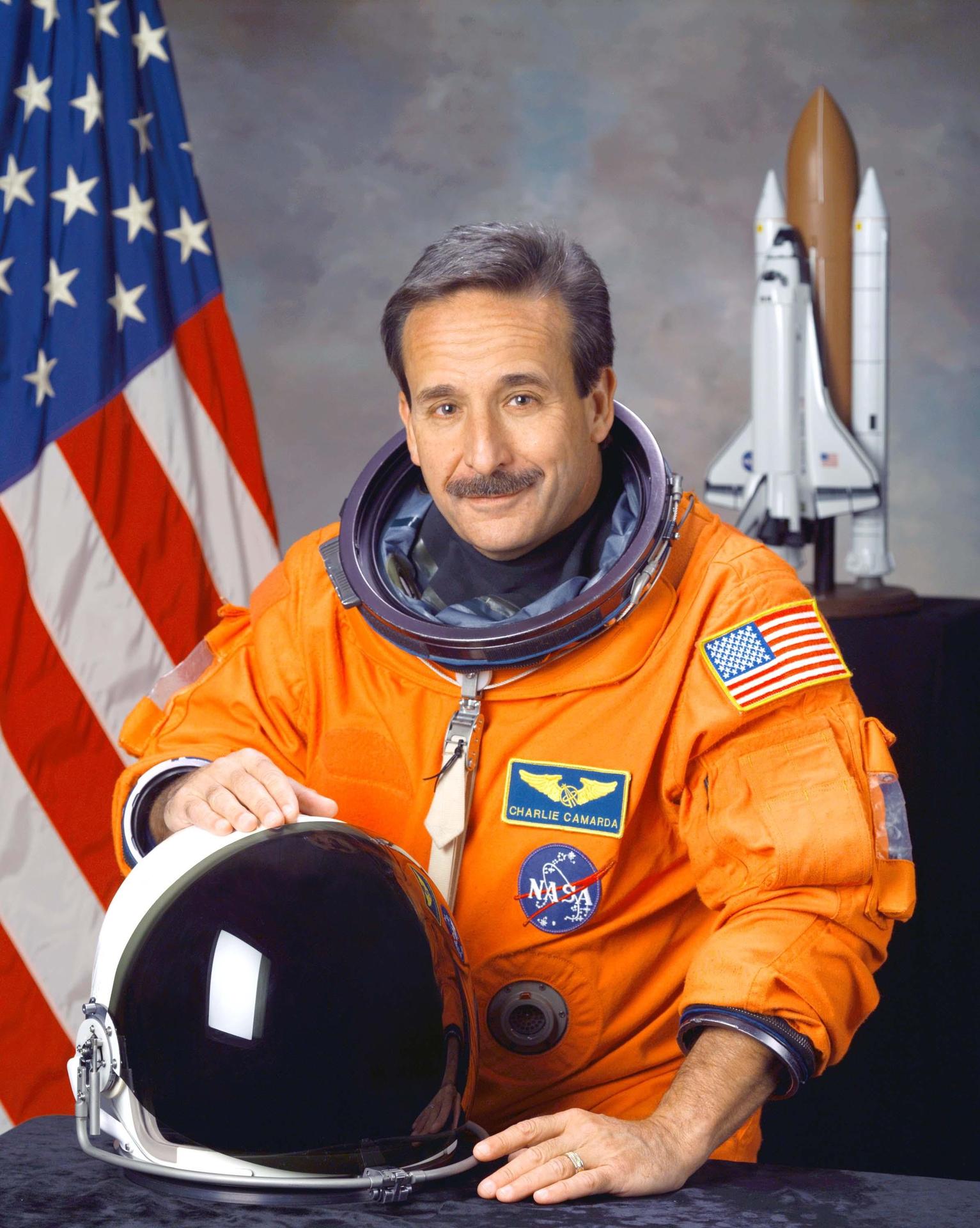 A man wearing a spacesuit sits and holds his helment in front of himself