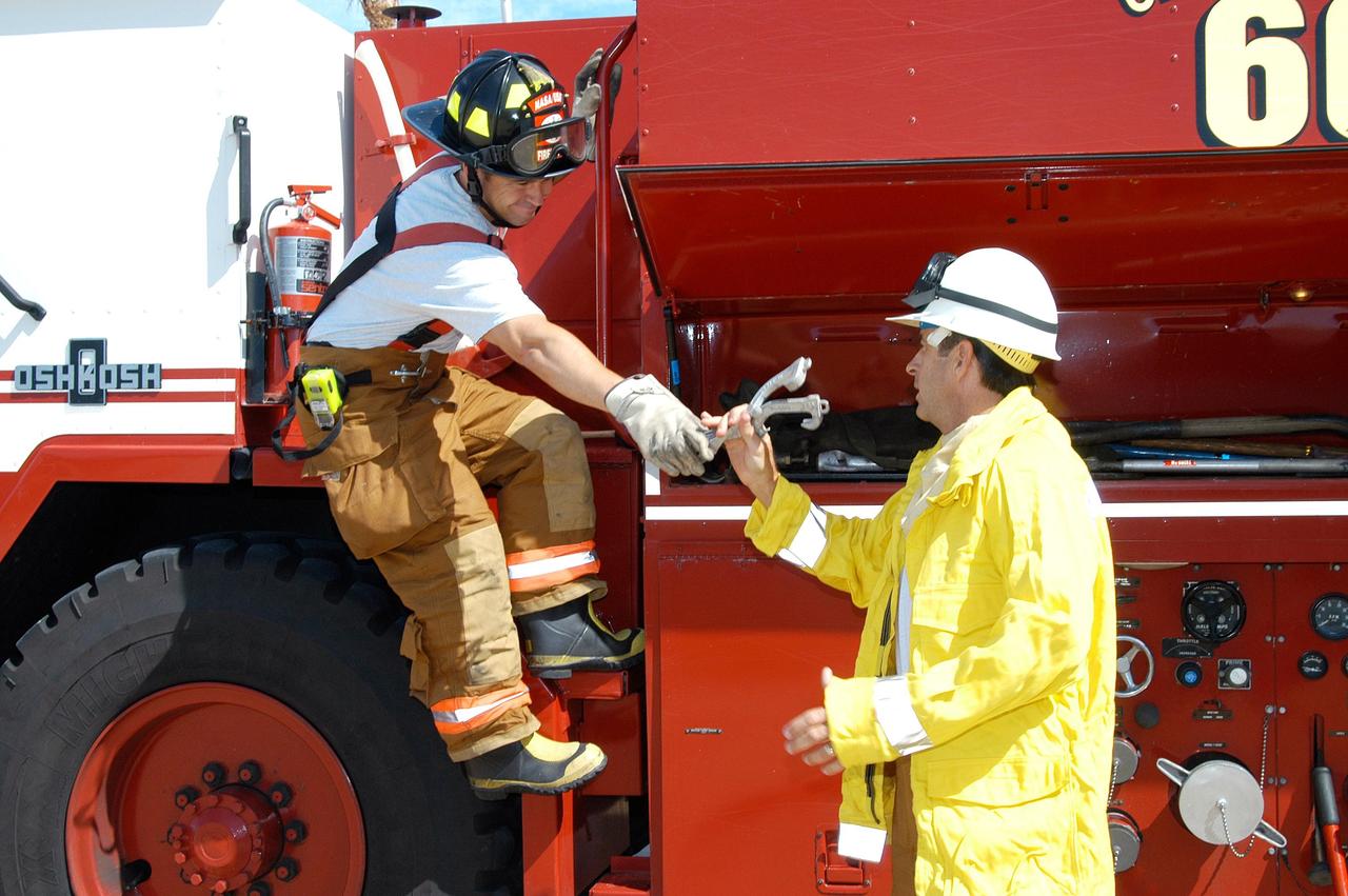KENNEDY SPACE CENTER, FLA.  -  At Cape Canaveral Air Force Station, KSC Firefighter Chris Maupin (left) takes equipment from Lt. Keith Abell.  They and other KSC firefighters teamed up with task forces from Satellite Beach, Malabar, Melbourne, Palm Bay, Patrick Air Force Base and Brevard County to help fight wildfires in the Palm Bay and Malabar areas that threatened homes and property during the Memorial Day holiday weekend.