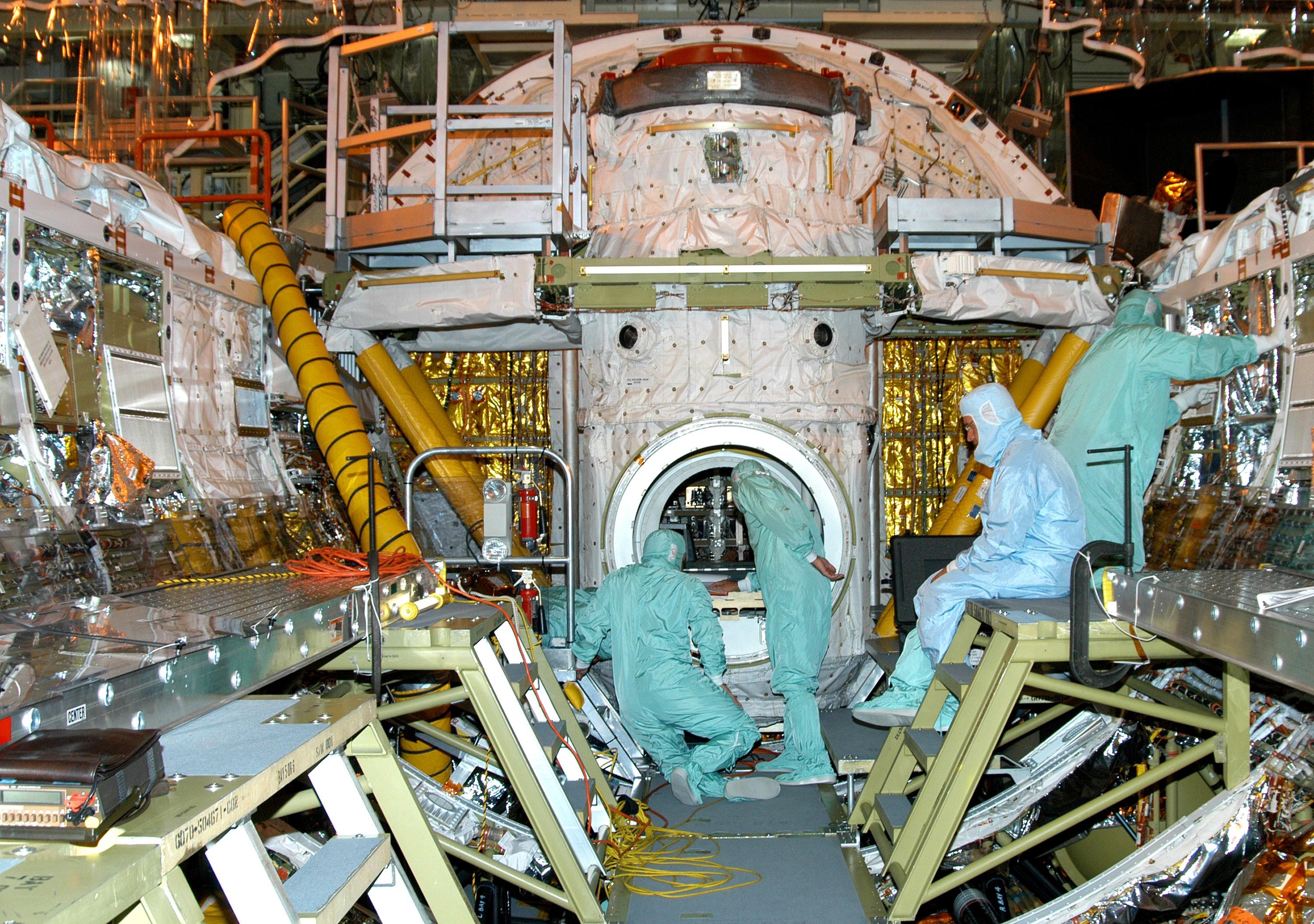 KENNEDY SPACE CENTER, FLA.  - In the Orbiter Processing Facility, two workers (center) check paperwork about the wiring being installed in Discovery’s cargo bay that will support the addition of an Orbiter Boom Sensor System (OBSS) .  The OBSS is one of the new safety measures for Return to Flight, equipping the Shuttle with cameras and laser systems to inspect the Shuttle’s Thermal Protection System while in space.  Discovery is designated as the Return to Flight vehicle for mission STS-114, no earlier than March 2005.