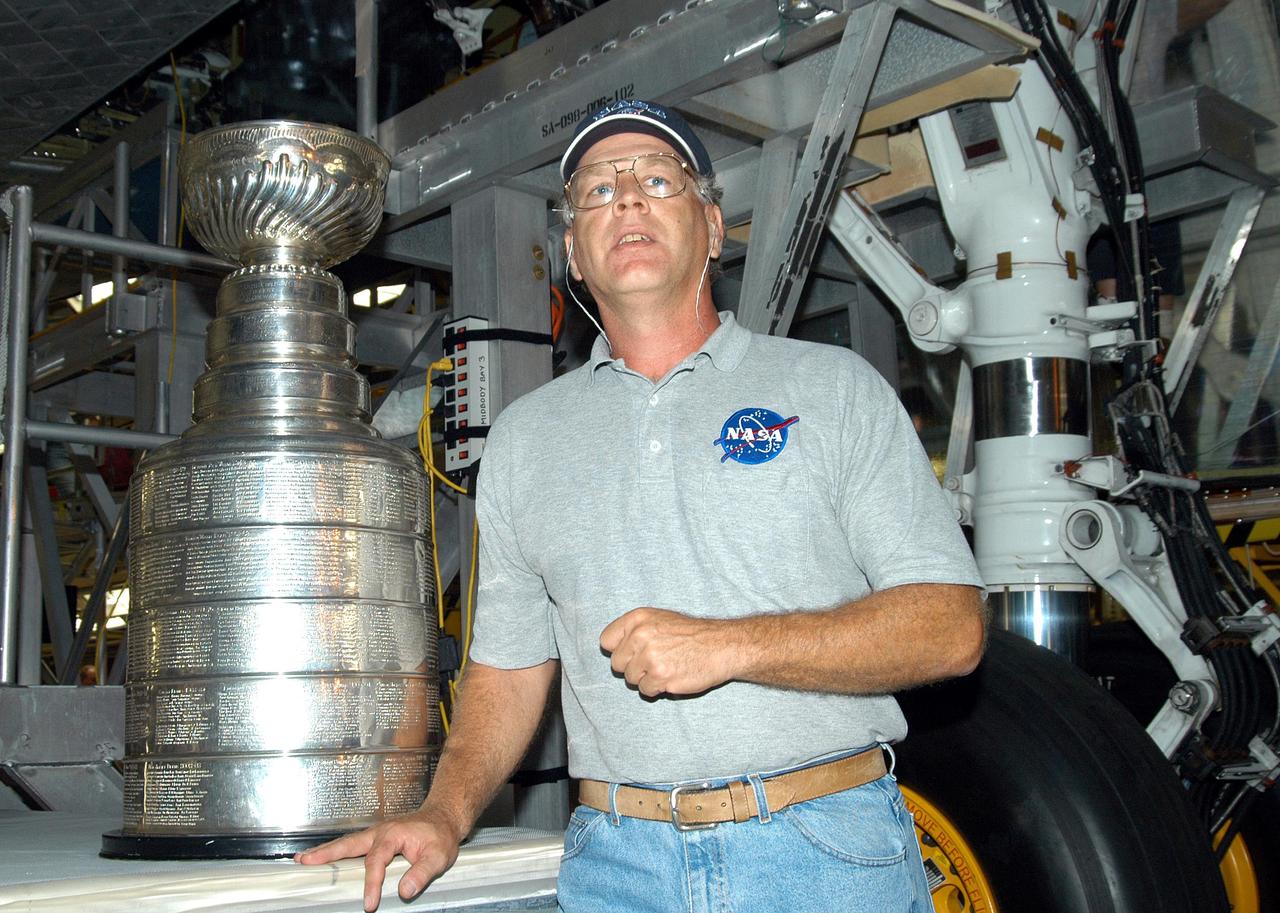 KENNEDY SPACE CENTER, FLA. - Jack Legere, NASA Quality Assurance specialist for the Shuttle Program, displays the Stanley Cup to employees in the Orbiter Processing Facility. Behind him is Discovery. Jay Feaster, general manager of the National Hockey League 2004 Champions Tampa Bay Lightning, brought the cup to KSC while on a tour. The cup was also briefly available for viewing by employees in the KSC Training Auditorium. The Stanley Cup weighs 35 pounds and is more than 100 years old. The Lightning will be added to the cup in September.