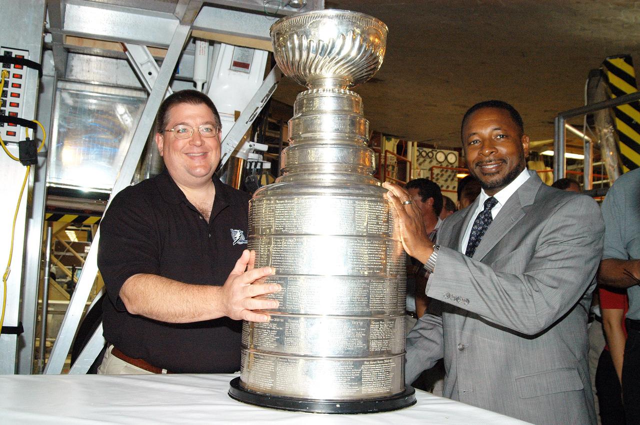 KENNEDY SPACE CENTER, FLA. - In the Orbiter Processing Facility, Jay Feaster, general manager of the National Hockey League 2004 Champions Tampa Bay Lightning, displays the Stanley Cup. At right is KSC Deputy Director Woodrow Whitlow. The cup was also briefly available for viewing by employees in the KSC Training Auditorium. Feaster brought the cup to KSC while on a tour. The Stanley Cup weighs 35 pounds and is more than 100 years old. The Lightning will be added to the cup in September.