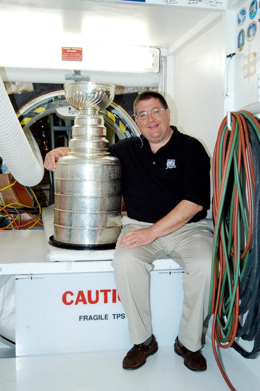KENNEDY SPACE CENTER, FLA. - In the Orbiter Processing Facility, Jay Feaster, general manager of the National Hockey League 2004 Champions Tampa Bay Lightning, sits next to the Stanley Cup in front of the open hatch into Discovery. The cup was also briefly available for viewing by employees in the KSC Training Auditorium. Feaster brought the cup to KSC while on a tour. The Stanley Cup weighs 35 pounds and is more than 100 years old. The Lightning will be added to the cup in September.
