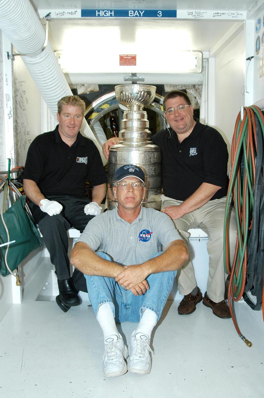 KENNEDY SPACE CENTER, FLA.  - Sitting in front of the open hatch into Discovery, which is in the Orbiter Processing Facility, Mike Bolt (left), NASA’s Jack Legere (center front) and Jay Feaster (right) display the Stanley Cup.  Feaster is general manager of the Tampa Bay Lightning, who won the cup in 2004, and Bolt is keeper of the cup.  Legere is NASA Quality Assurance specialist for the Shuttle Program.  The cup was also briefly available for viewing by employees in the KSC Training Auditorium.  Feaster brought the cup to KSC while on a tour.  The Stanley Cup weighs 35 pounds and is more than 100 years old.  The Lightning will be added to the cup in September.