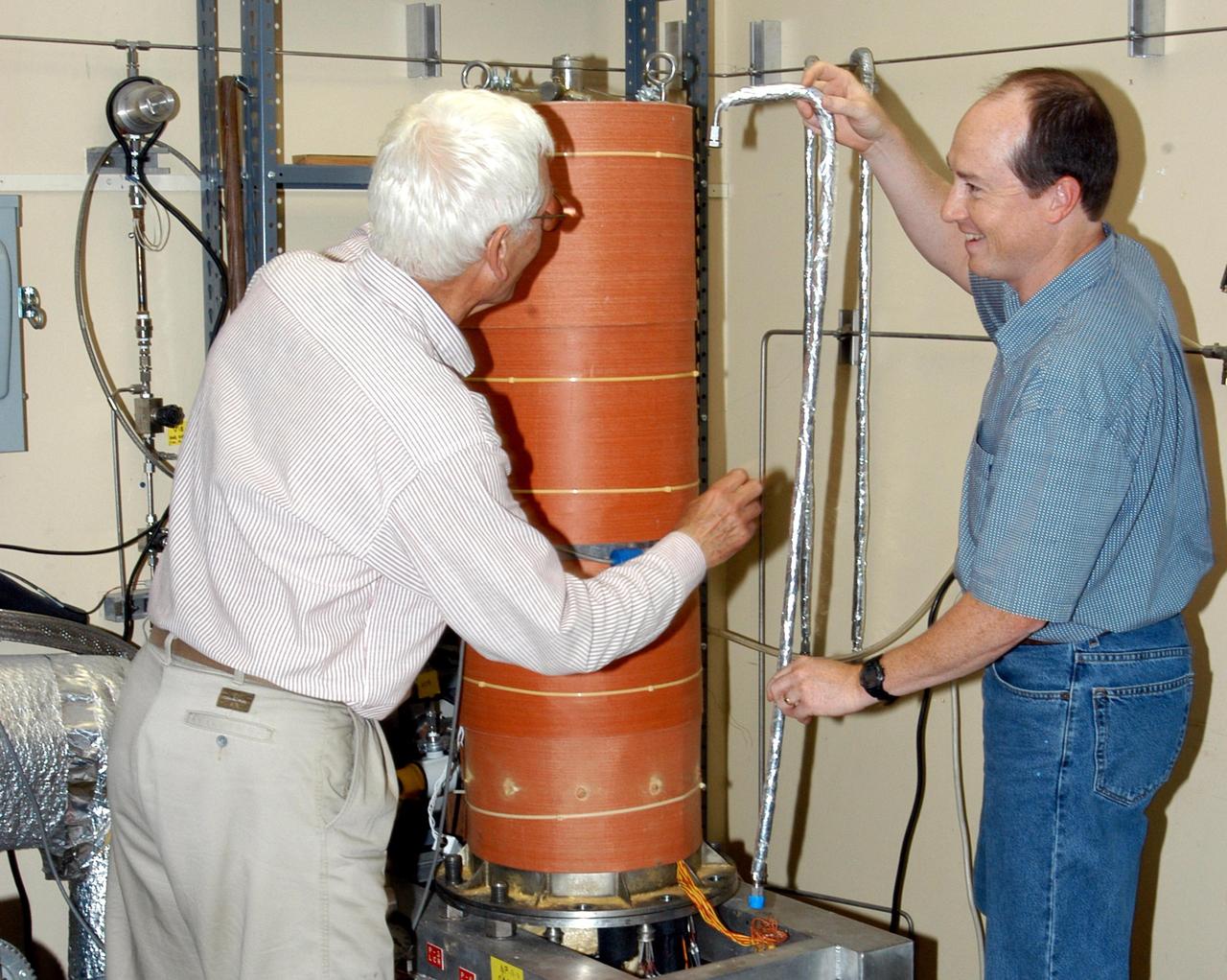 KENNEDY SPACE CENTER, FLA. -  James E. Fesmire (right), NASA lead engineer for the KSC Cryogenics Testbed, works on Cryostat-1, the Methods of Testing Thermal Insulation and Association Test Apparatus, which he developed.  At left is co-inventor Dr. Stan Augustynowicz, chief scientist with Sierra Lobo Inc. in Milan, Ohio. Cryostat-1 provides absolute thermal performance values of cryogenic insulation systems under real-world conditions. Cryogenic liquid is supplied to a test chamber and two guard chambers, and temperatures are sensed within the vacuum chamber to test aerogels, foams or other materials.   The Cryostat-1 machine can detect the absolute heat leakage rates through materials under the full range of vacuum conditions. Fesmire recently acquired three patents for testing thermal insulation materials for cryogenic systems. The research team of the Cryogenics Testbed offers testing and support for a number of programs and initiatives for NASA and commercial customers.