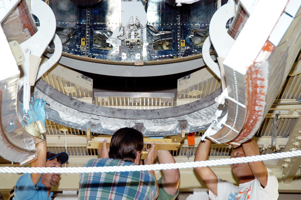 KENNEDY SPACE CENTER, FLA. - Workers in the Orbiter Processing Facility lift the Reinforced Carbon-Carbon (RCC) chin panel into place on Discovery. The chin panel is the smile-shaped section of RCC directly below the nose cap that provides a thermal barrier during re-entry.  The nose cap, with chin panel, was removed from the vehicle in the summer of 2003 and returned to the vendor, where it underwent numerous forms of Non-Destructive Evaluation.  These tests included X-ray, ultrasound and eddy current to ensure its structural integrity prior to reinstallation.  Discovery is designated as the Return to Flight vehicle for mission STS-114, no earlier than March 2005.