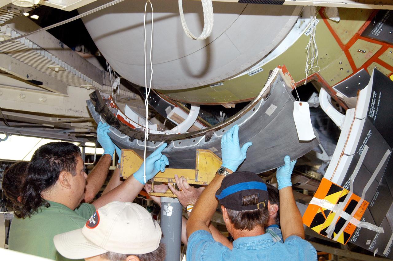 KENNEDY SPACE CENTER, FLA. - Workers in the Orbiter Processing Facility check the placement of the Reinforced Carbon-Carbon (RCC) chin panel on Discovery.  .  The chin panel is the smile-shaped section of RCC directly below the nose cap that provides a thermal barrier during re-entry.  The nose cap, with chin panel, was removed from the vehicle in the summer of 2003 and returned to the vendor, where it underwent numerous forms of Non-Destructive Evaluation.  These tests included X-ray, ultrasound and eddy current to ensure its structural integrity prior to reinstallation.  Discovery is designated as the Return to Flight vehicle for mission STS-114, no earlier than March 2005.