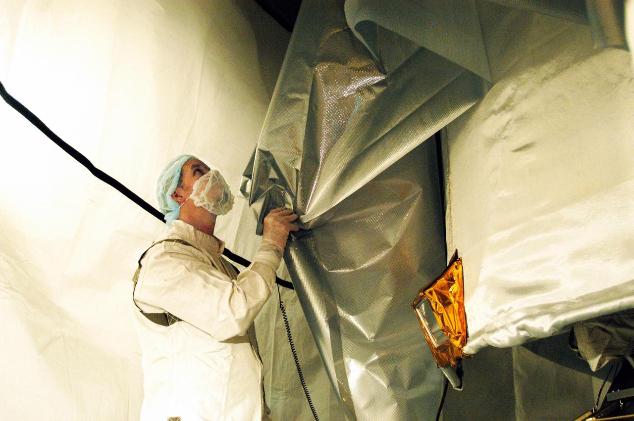 KENNEDY SPACE CENTER, FLA. - Inside the environmental curtain suspended around the MESSENGER (Mercury Surface, Space Environment, Geochemistry and Ranging) spacecraft while in the mobile service tower at Launch Complex 17-B, Cape Canaveral Air Force Station, a worker removes the protective material wrapped around MESSENGER. Visible at right is the sunshade that will protect MESSENGER’s instruments during exposure to the sun as it orbits Mercury. Scheduled to launch Aug. 2, MESSENGER will return to Earth for a gravity boost in July 2005, then fly past Venus twice, in October 2006 and June 2007. It is expected to enter Mercury orbit in March 2011. MESSENGER was built for NASA by the Johns Hopkins University Applied Physics Laboratory in Laurel, Md. Processing is being done at Astrotech Space Operations in Titusville, Fla.