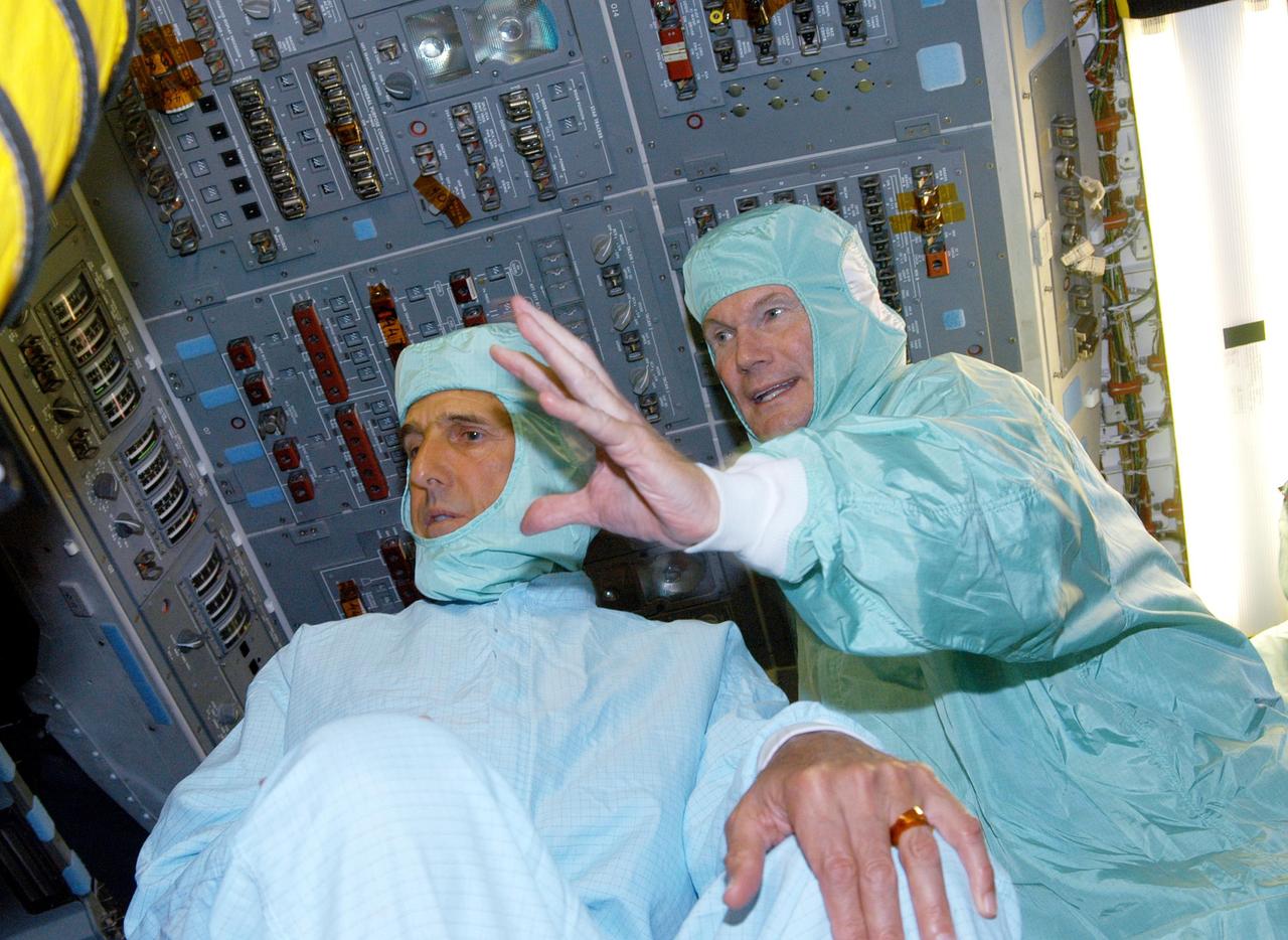 KENNEDY SPACE CENTER, FLA. - Sen. Bill Nelson (right), D-Fla., explains the layout of the glass cockpit to Sen. John F. Kerry, D-Mass., on the flight deck of orbiter Discovery during a tour of the Orbiter Processing Facility (OPF). The “bunny suits” they are wearing are clean room attire required for anyone coming in close proximity to Discovery, currently being prepared for flight on the next Space Shuttle mission. The tour of the OPF follows a public meeting Kerry held at the Dr. Kurt H. Debus Conference Facility at the Kennedy Space Center Visitor Complex.  He said he chose to speak at KSC because it symbolizes America’s commitment to science, innovation and technology. He and Sen. John Edwards, D-N.C., are on a speaking tour prior to their appearance at the Democratic National Convention in Boston.