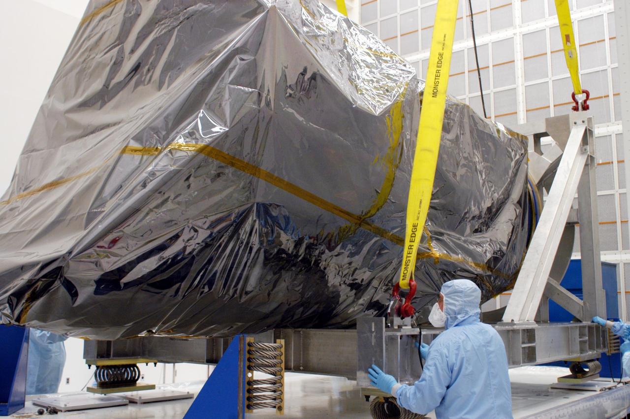 KENNEDY SPACE CENTER, FLA. - Inside Hangar AE at Cape Canaveral Air Force Station (CCAFS), workers attach straps from an overhead crane onto the platform under the Swift spacecraft, which is enclosed in a protective cover. Swift will be raised to vertical and placed on a work stand. Swift is a first-of-its-kind, multi-wavelength observatory dedicated to the study of gamma-ray burst (GRB) science. Its three instruments will work together to observe GRBs and afterglows in the gamma-ray, X-ray and optical wavebands. Swift is part of NASA’s medium explorer (MIDEX) program being developed by an international collaboration. It will be launched no earlier than Oct. 7 into a low-Earth orbit on a Boeing Delta 7320 rocket from pad 17-A at CCAFS. During its nominal 2-year mission, Swift is expected to observe more than 200 bursts, which will represent the most comprehensive study of GRB afterglow to date.